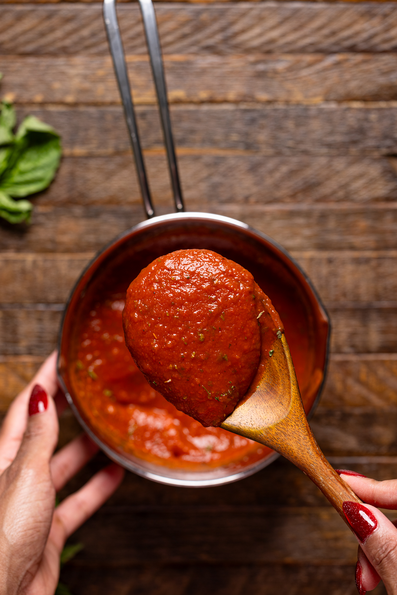 Image of pizza sauce in a saucepan and being held in a spoon by woman hands.