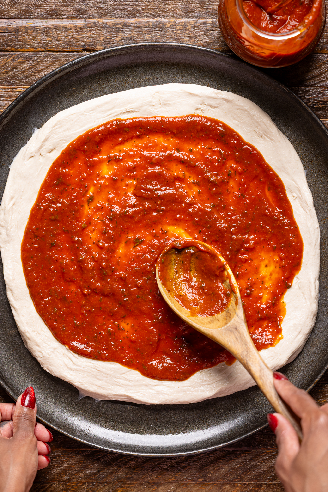 An image of pizza sauce being spooned on a pizza crust.