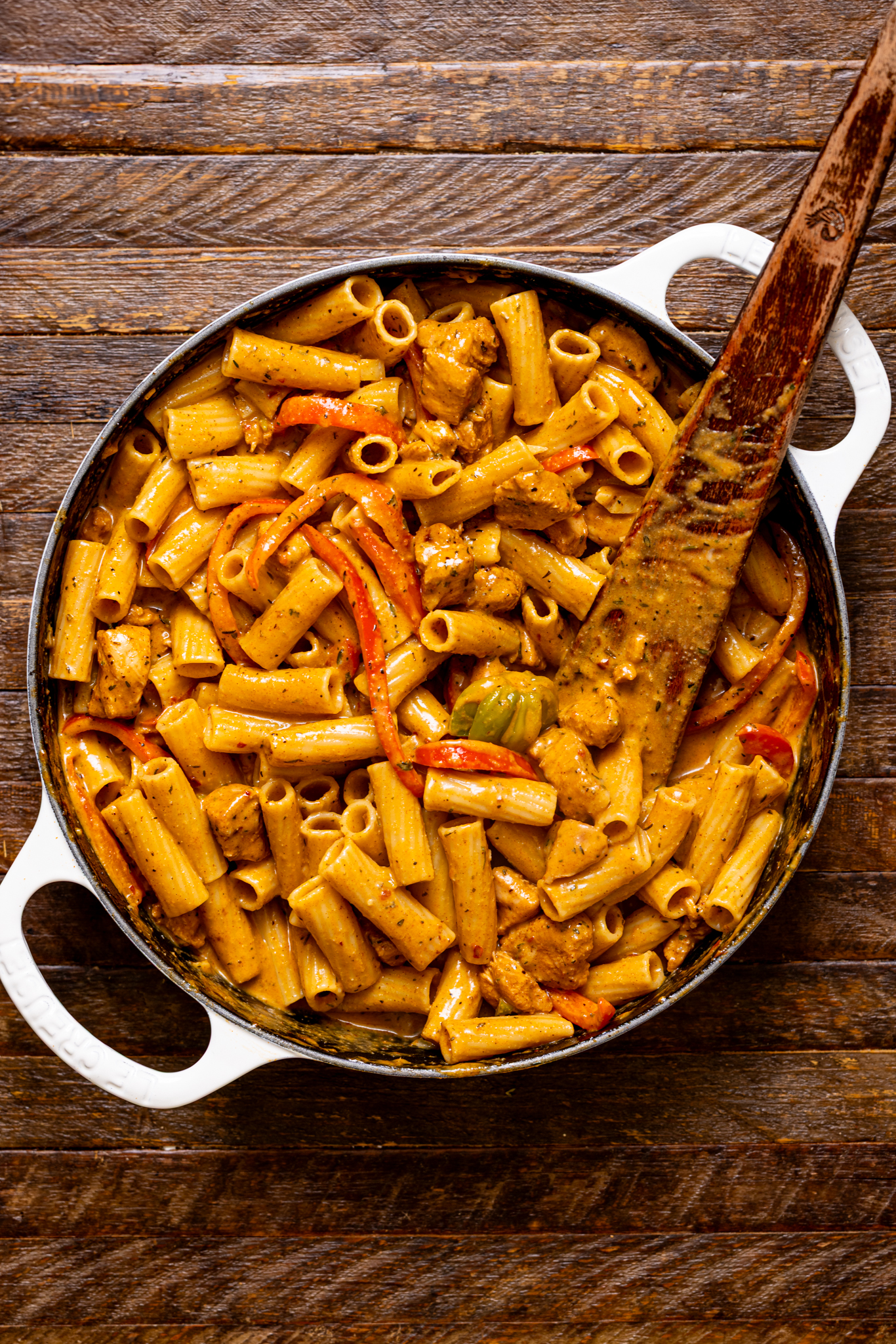 Authentic Jerk Chicken Rasta Pasta in a white skillet pot with a wooden spoon.