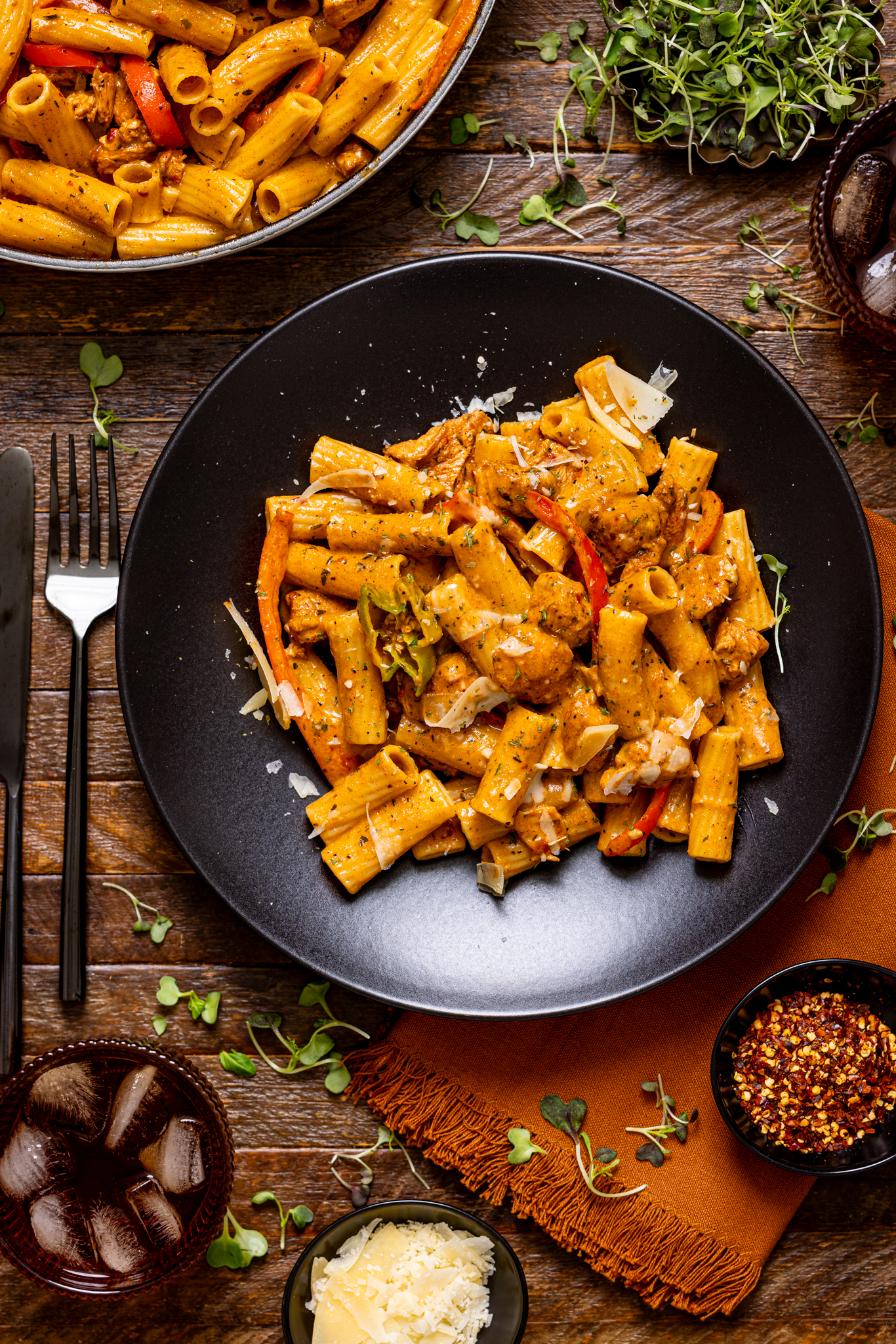 Jerk chicken rasta pasta on two black plates with drinks and utensils. 