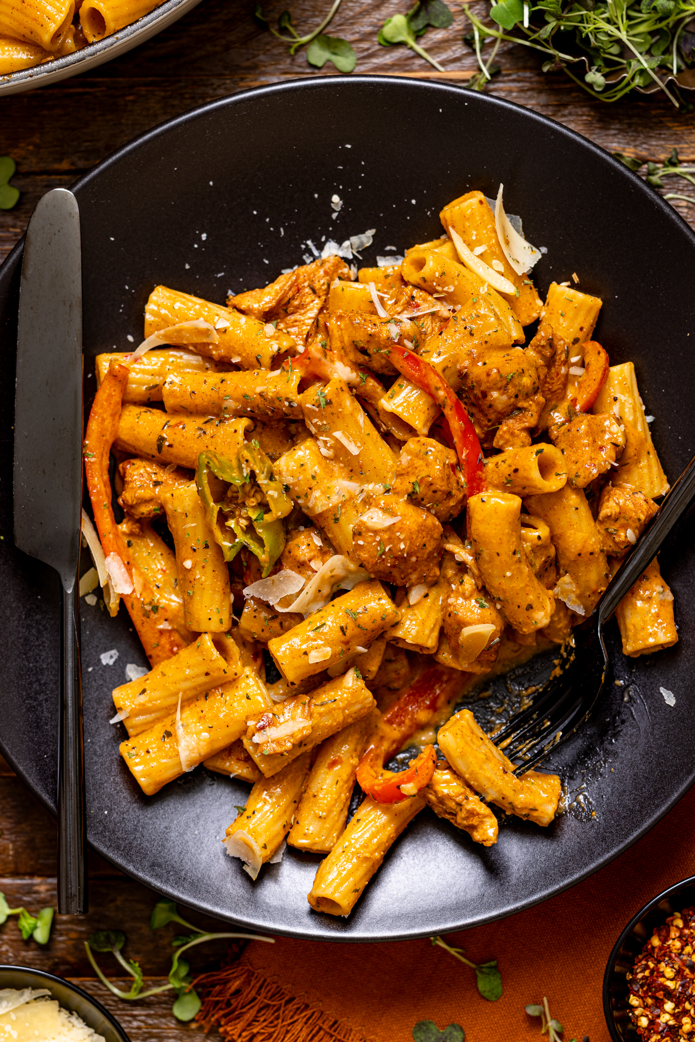 Up close shot of the Jerk Chicken Rasta Pasta on a plate with utensils. 