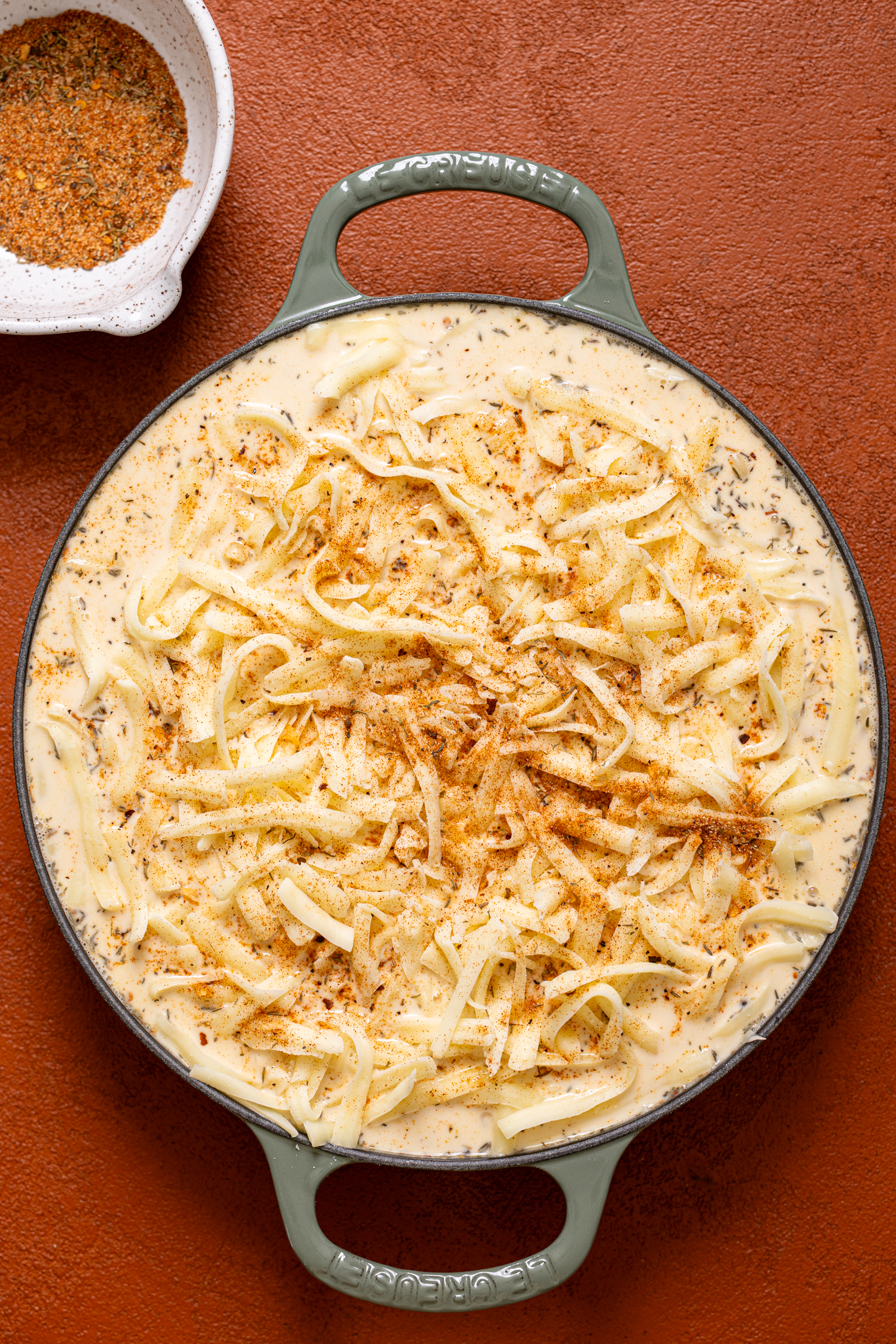 Ingredients together in a green skillet on a burnt orange table.