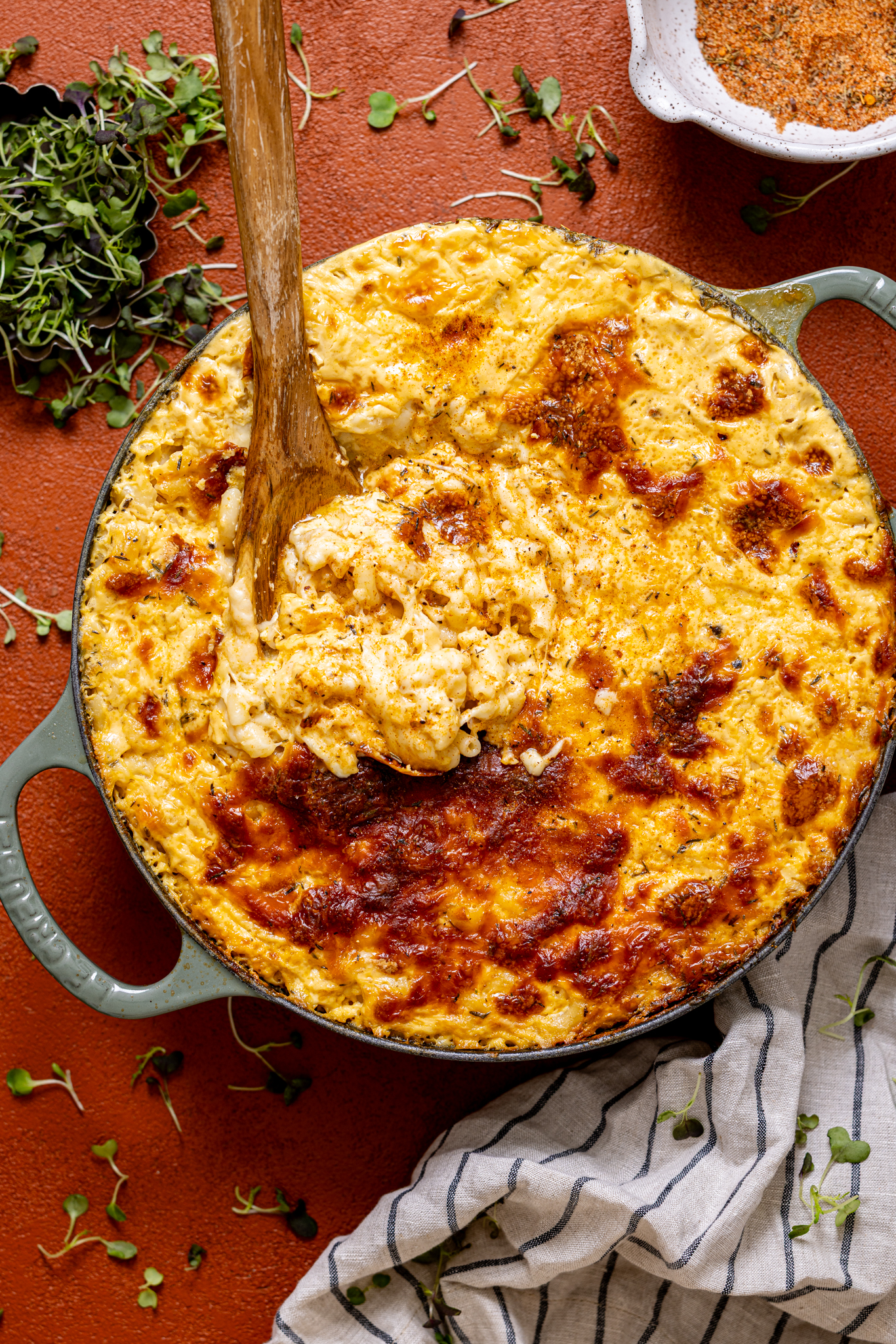 Baked Jerk Mac and Cheese in a green skillet with a wooden spoon.