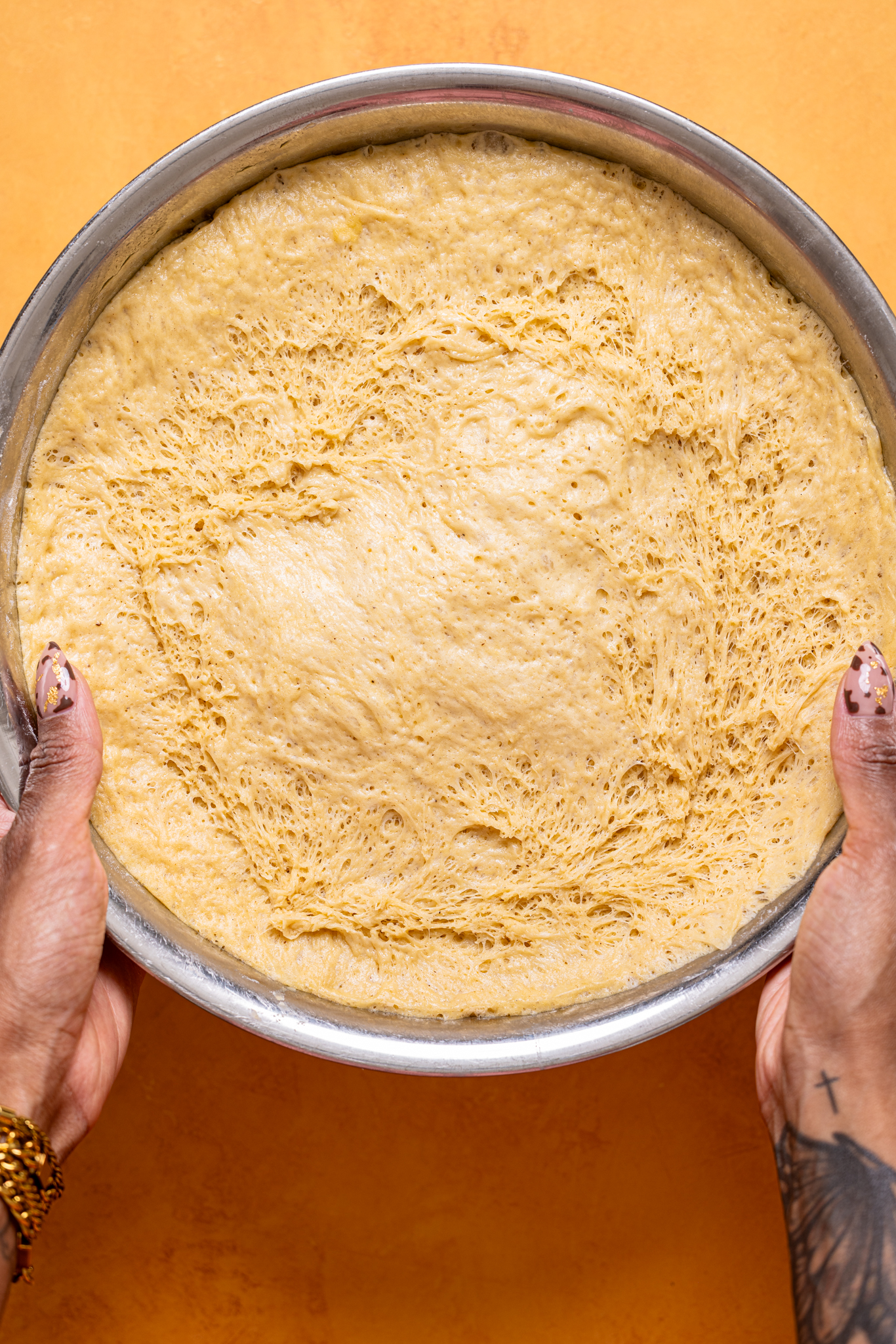 Risen dough in a silver bowl being held with woman hands.