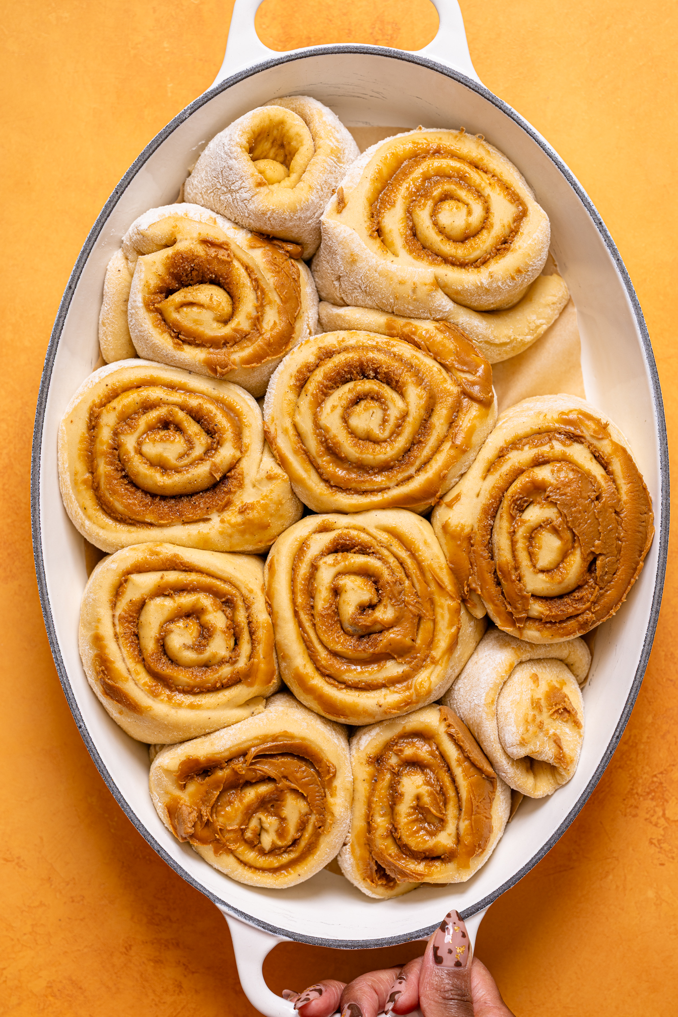 Assembled and shaped cinnamon rolls in a baking dish being held by woman hands.