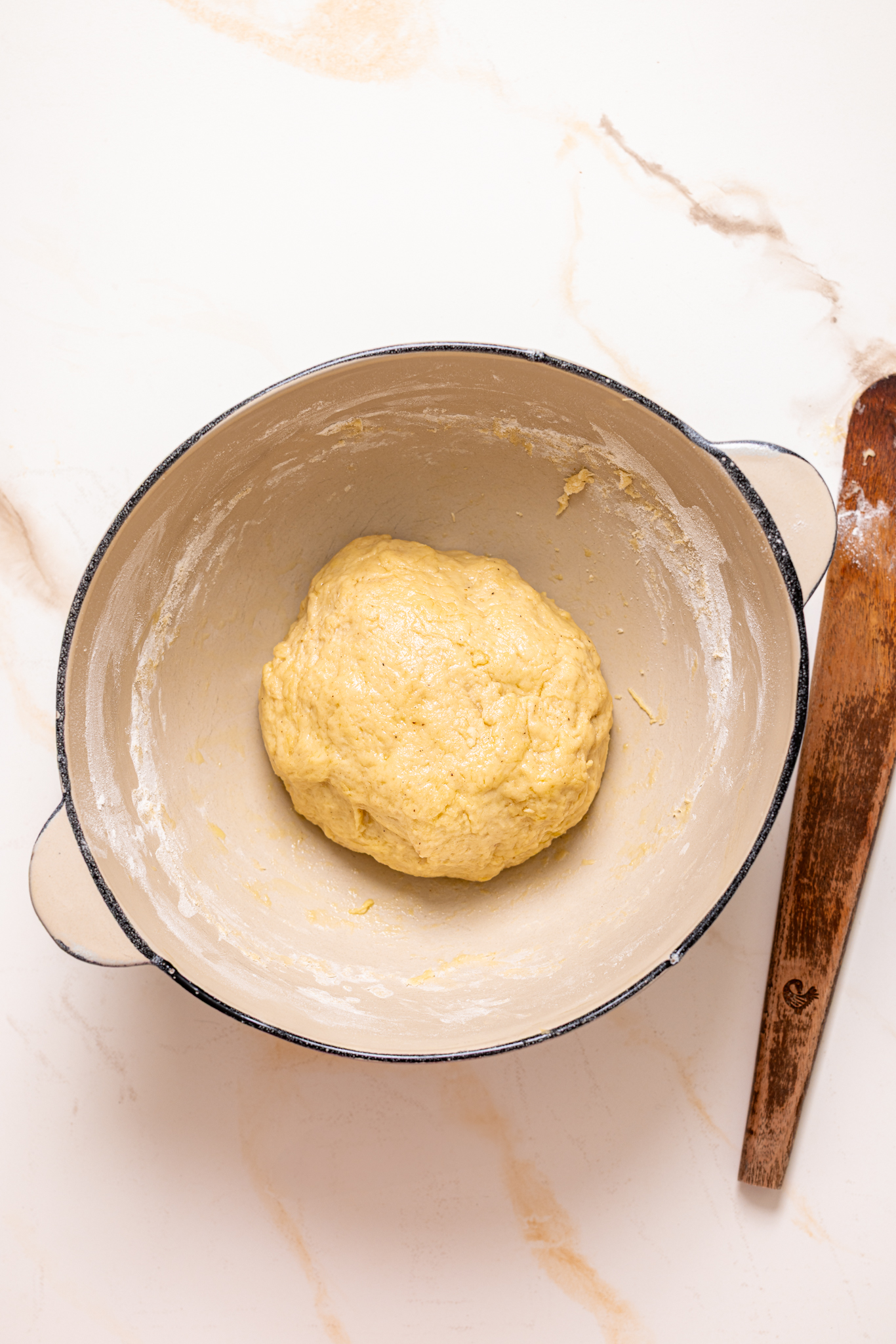 Cinnamon roll dough in a bowl on a marble table with a wooden rolling pin.