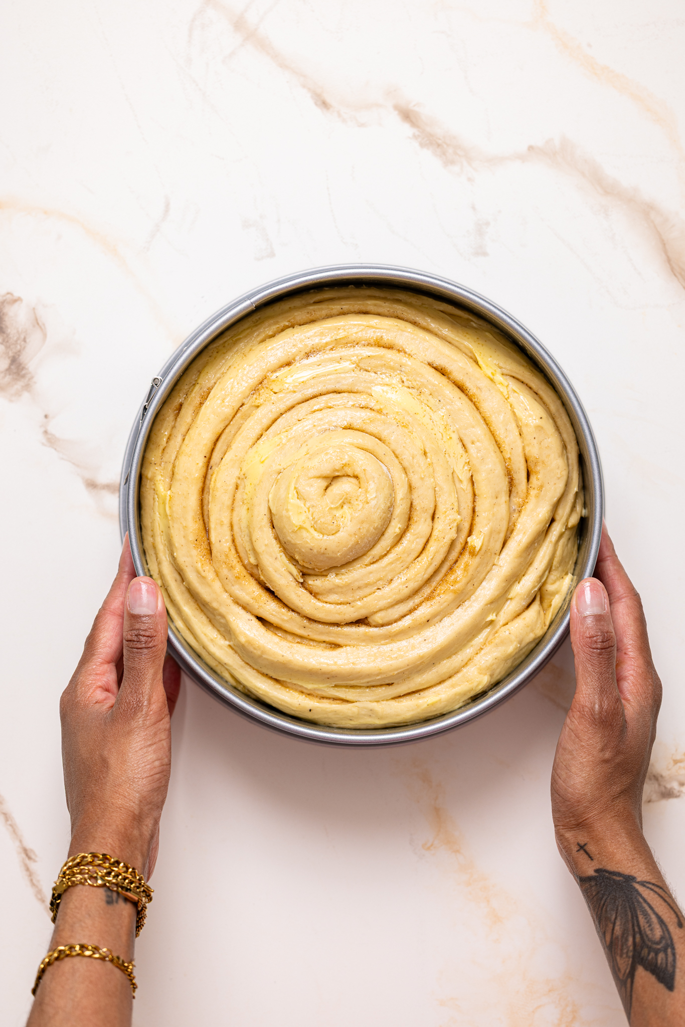Raised shaped dough in a baking pan being held with woman hands.