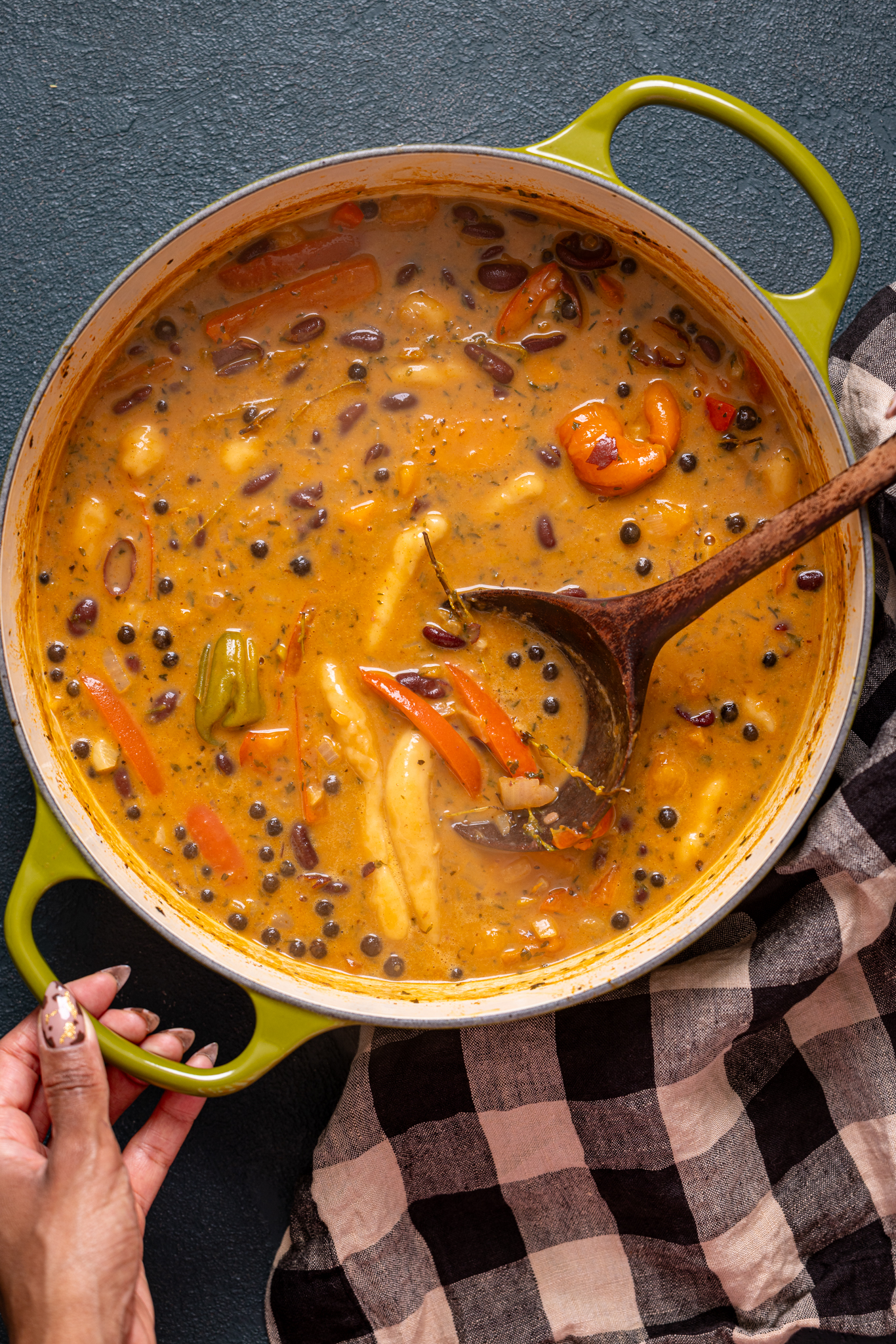 A large pot of Jamaican Vegan Red Peas soup with a wooden spoon being held with woman hands.