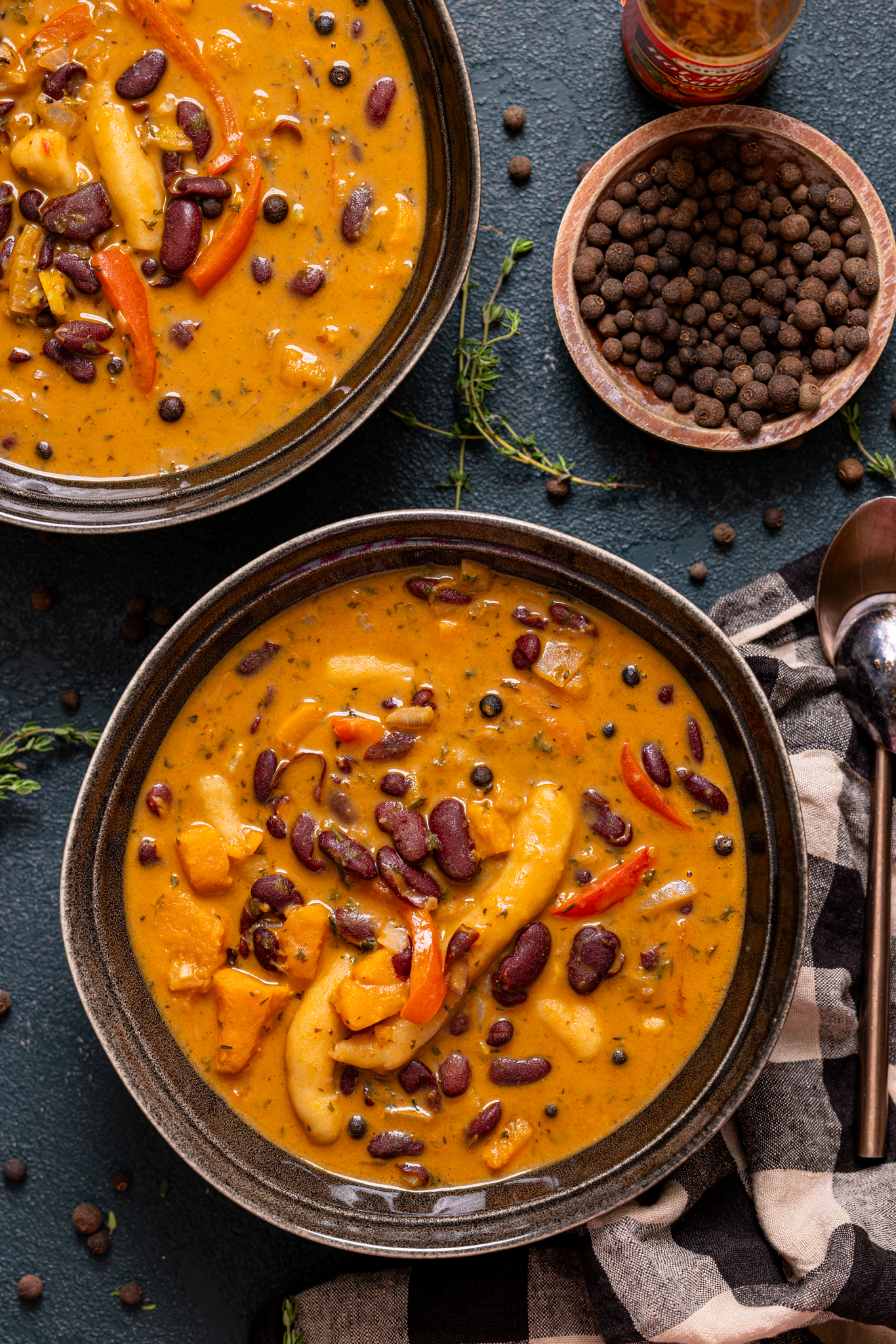 Vegan Red Peas soup in two bowls with allspice berries and hot sauce.