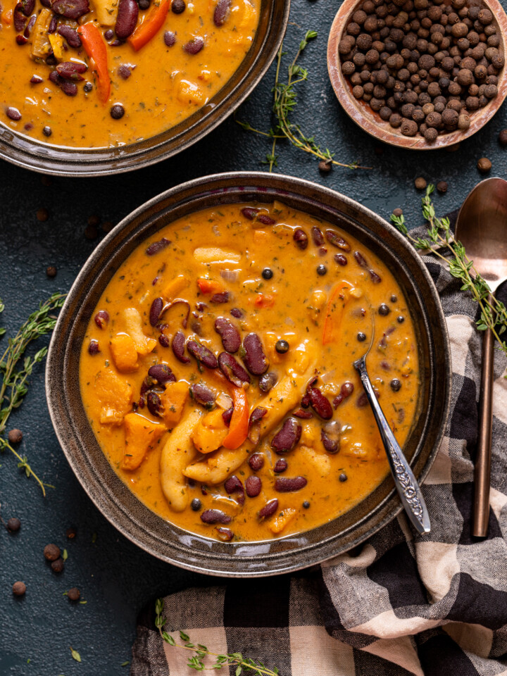 Two bowls of soup with spoons, allspice berries, and hot sauce.