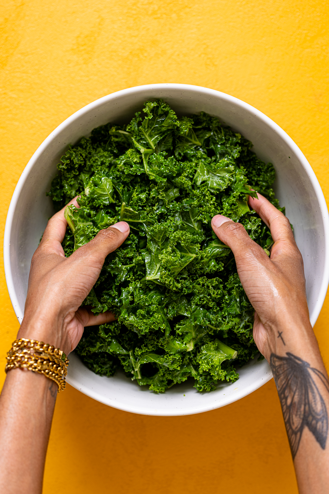 Kale being massaged in a white bowl by woman hands.