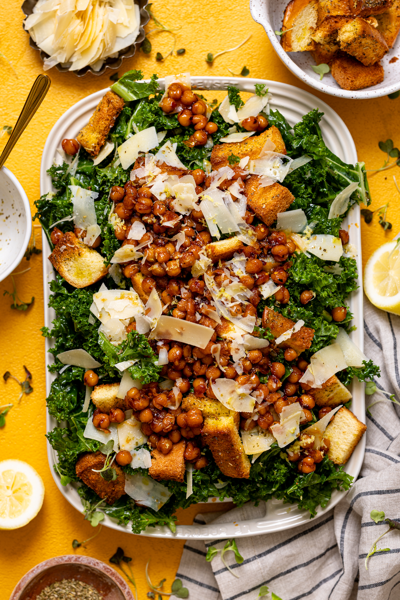 Lemon Parmesan Kale Salad with Hot Honey Chickpeas on a platter with garnish on a yellow table.