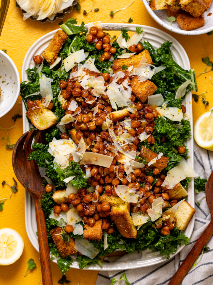 Salad on a platter with wooden serving utensils and garnishes.