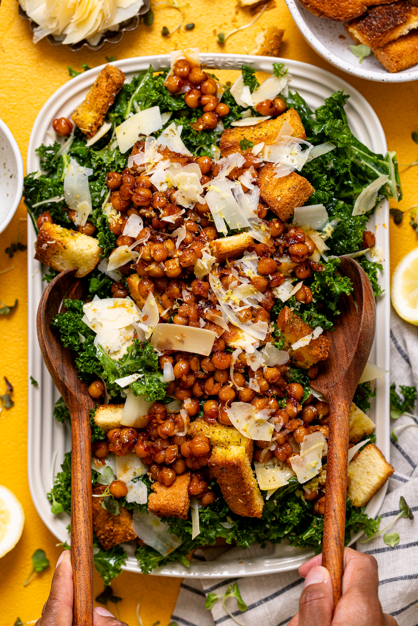 Kale salad being scooped up with wooden serving utensils held by woman hands.