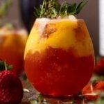 Glass of Mango Strawberry Smash Mocktail with strawberries and thyme sprigs.