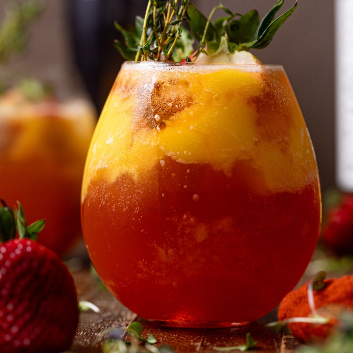 Glass of Mango Strawberry Smash Mocktail with strawberries and thyme sprigs.