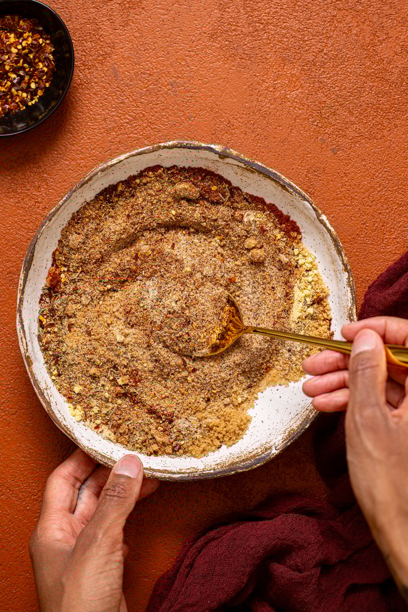 Seasoning in a bowl being stirred with a spoon by woman hands.