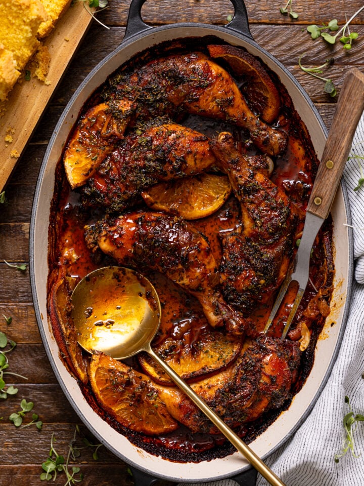 Southern Baked Maple Citrus Chicken Legs in a baking dish with serving utensils and side of cornbread.
