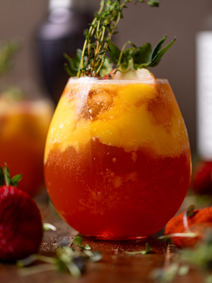 Glass of Mango Strawberry Smash Mocktail with strawberries and thyme sprigs.