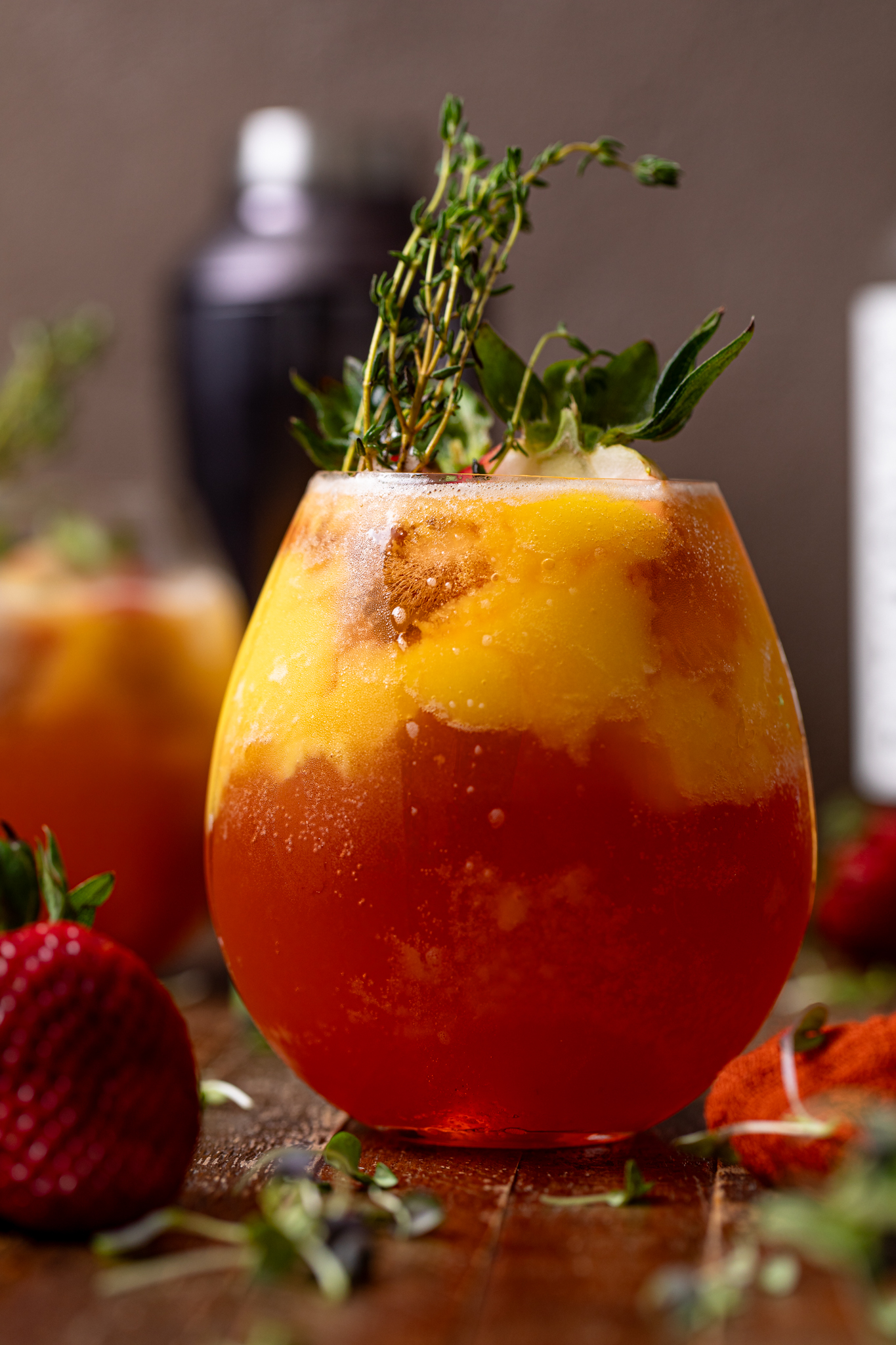 Glass of Mango Strawberry Smash Mocktail with strawberries and thyme sprigs.