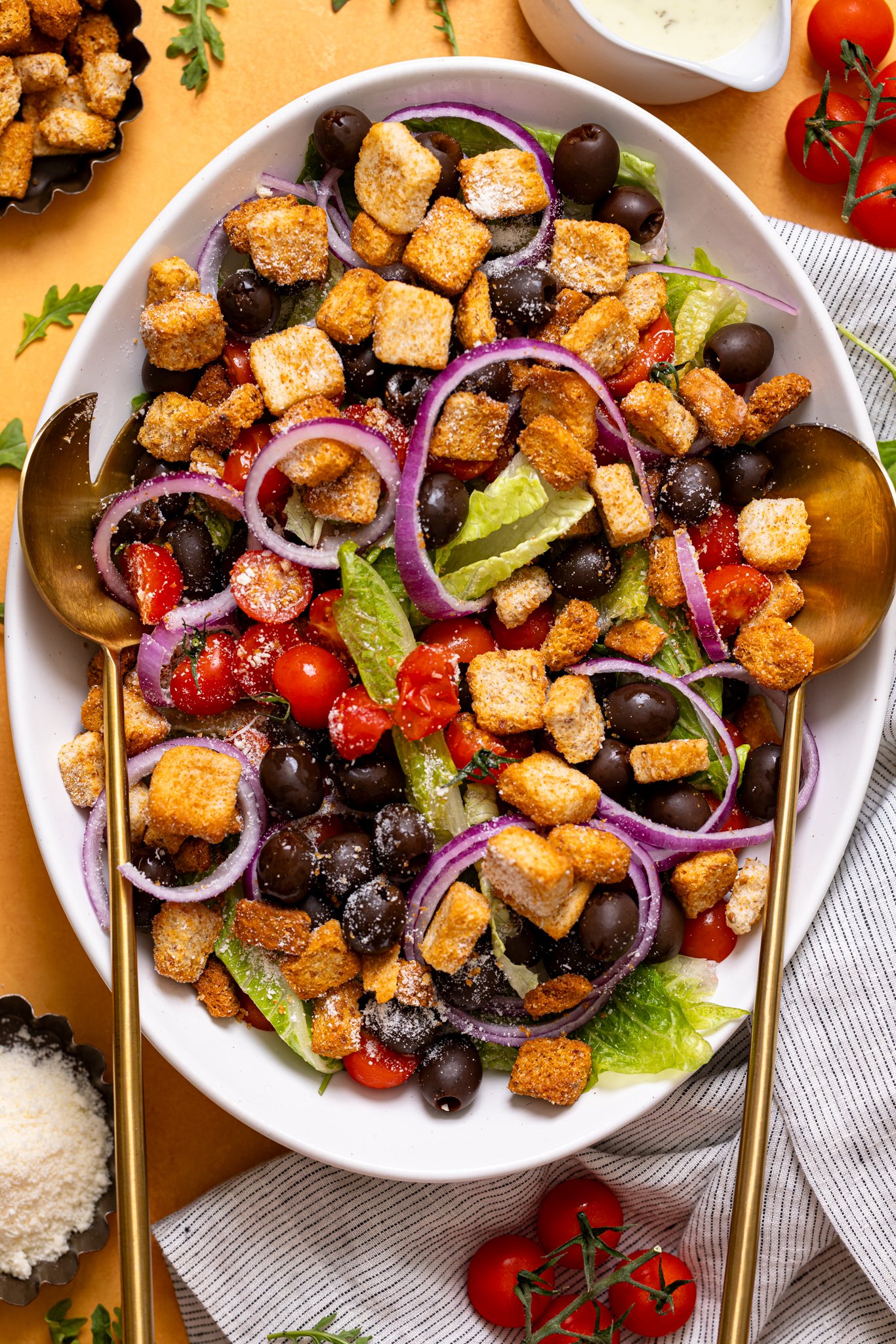 Copycat Olive Garden House Salad with Homemade Dressing on a white platter with serving utensils on a yellow table.