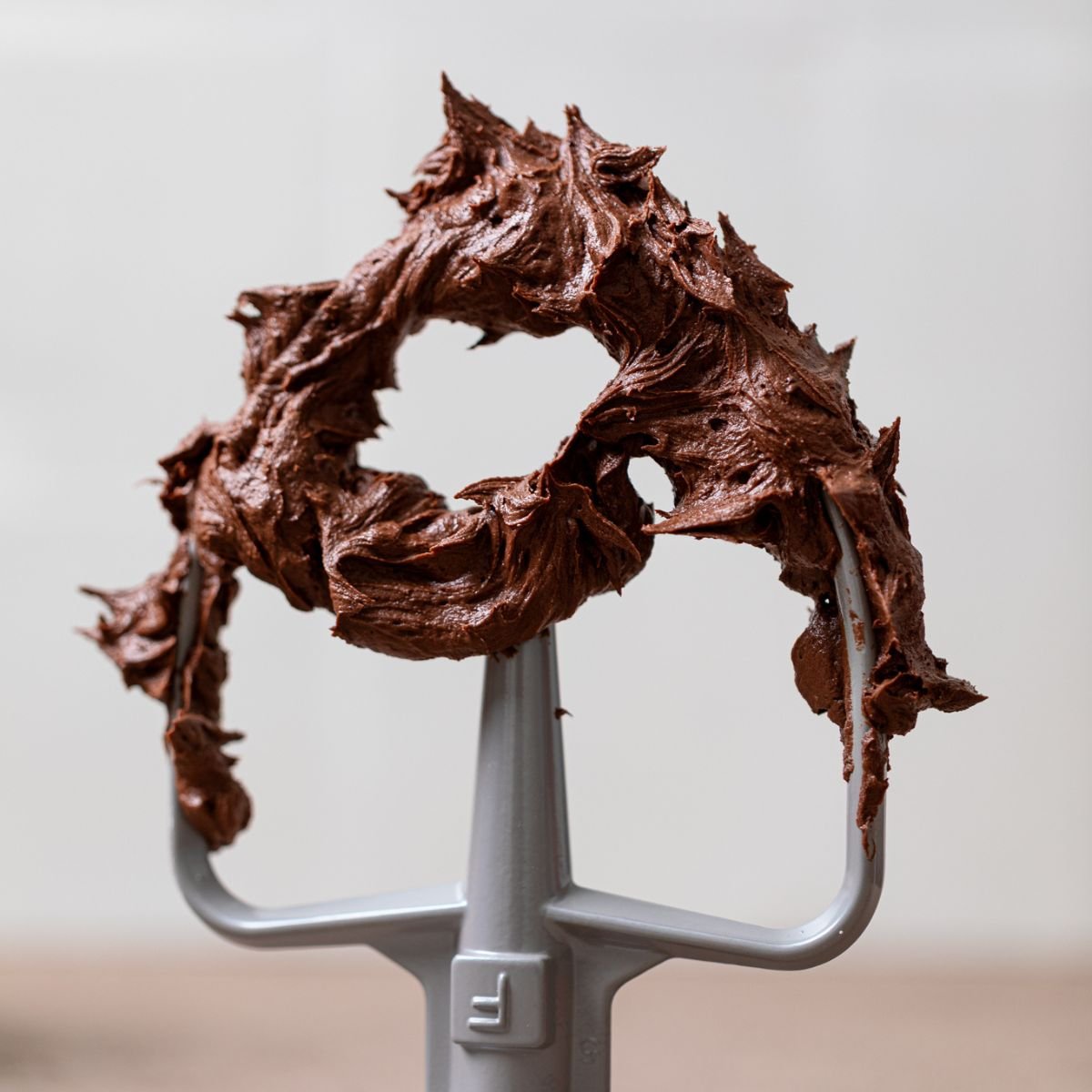 Easy Whipped Chocolate Buttercream Frosting on a mixer whisk standing on a table.