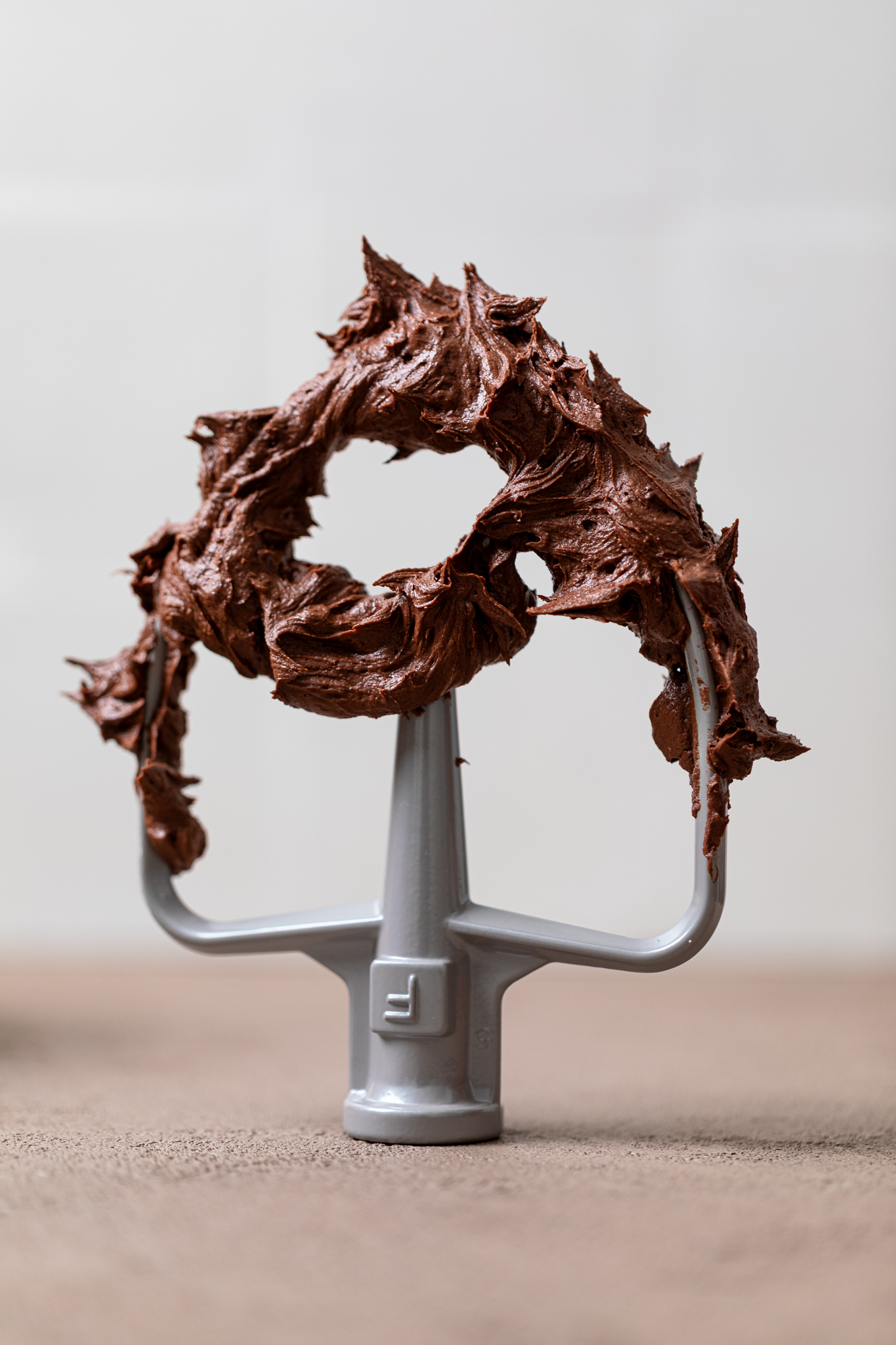 Easy Whipped Chocolate Buttercream Frosting on a mixer whisk standing on a table.