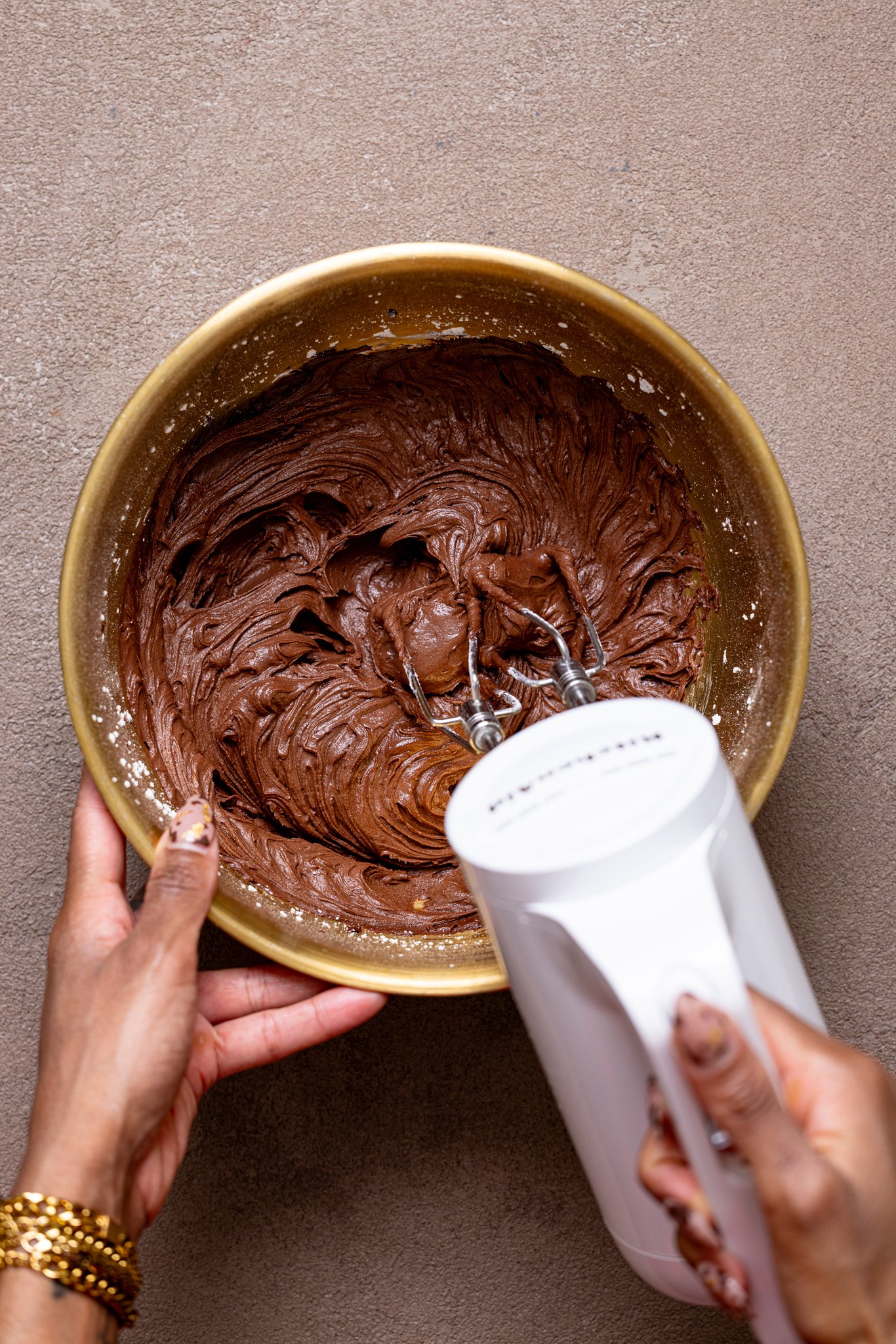 Easy Whipped Chocolate Buttercream Frosting being whipped in a bowl with a mixer by woman hands.