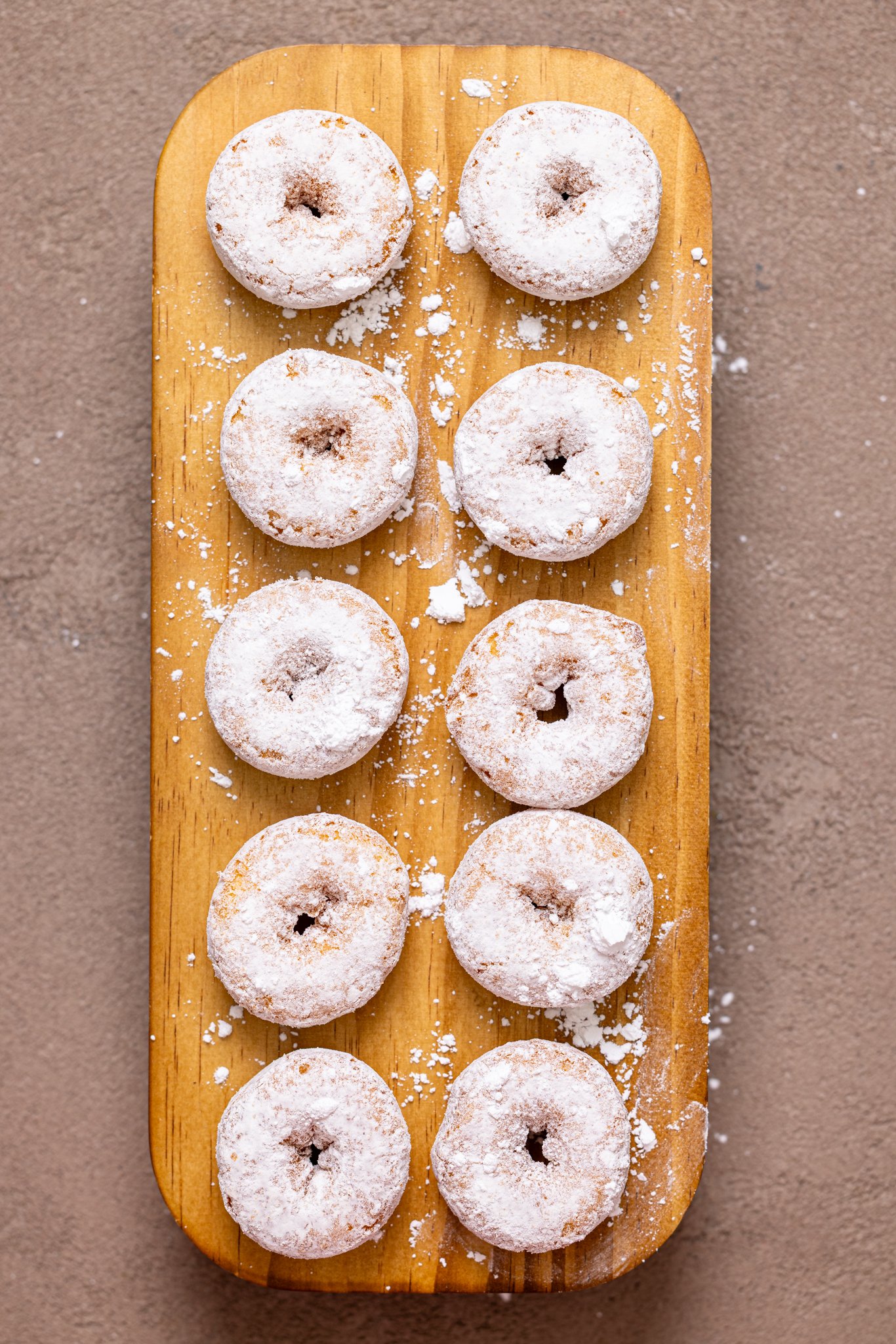 Homemade Mini Powdered Sugar Donuts lined up on a wood server.