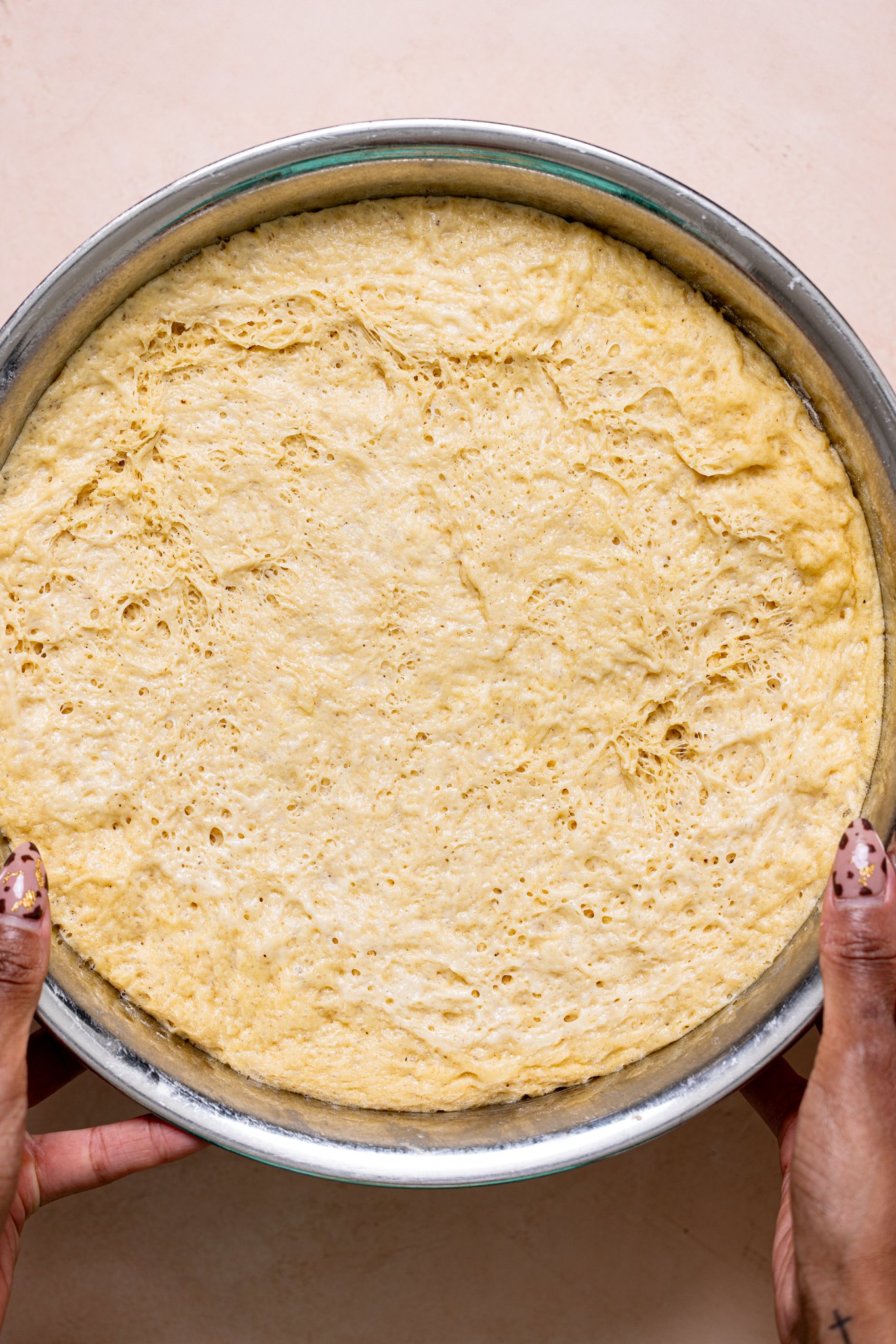 Dough in a bowl being held by woman hands.