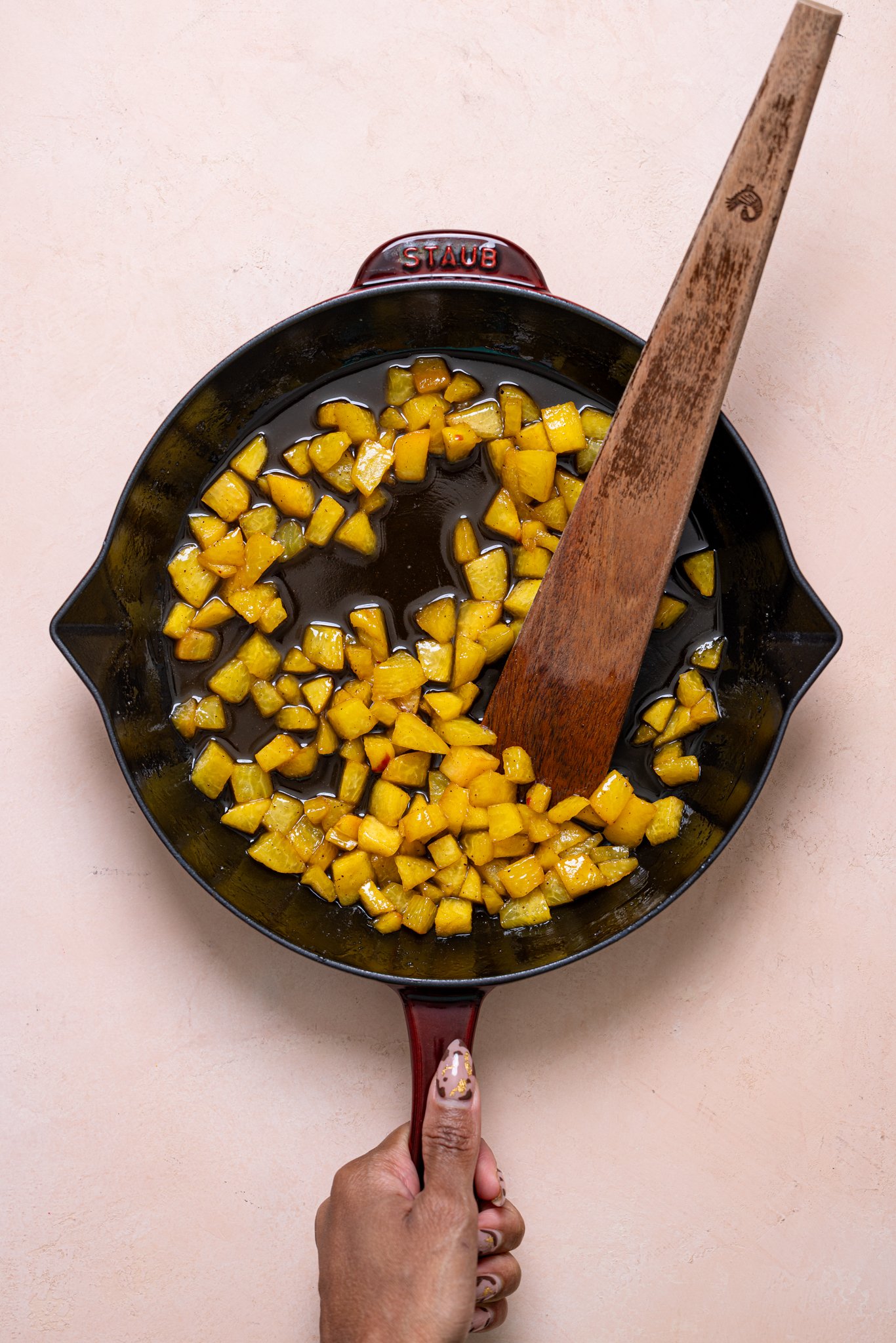 Diced peaches in a skillet with a wooden spoon.
