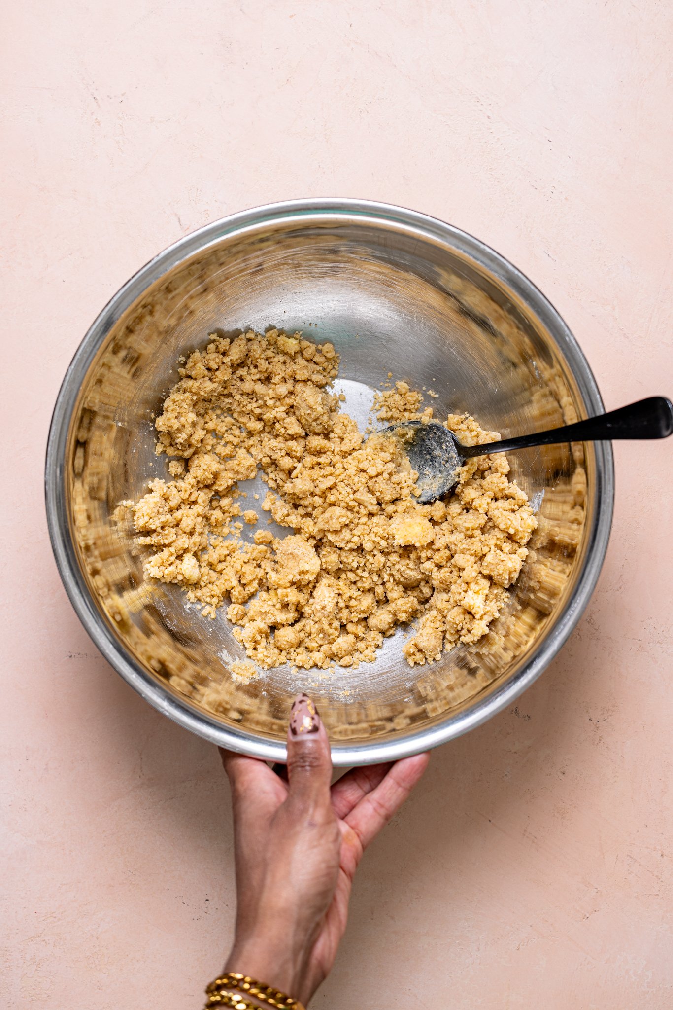 Crumble topping in a bowl with a spoon being held by woman hands.