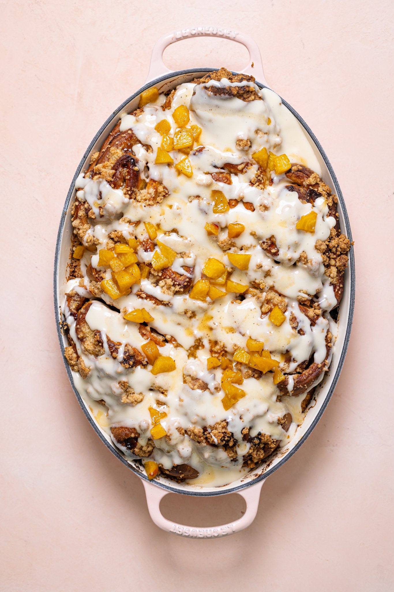 Baked cinnamon rolls in a  baking dish with frosting and toppings.