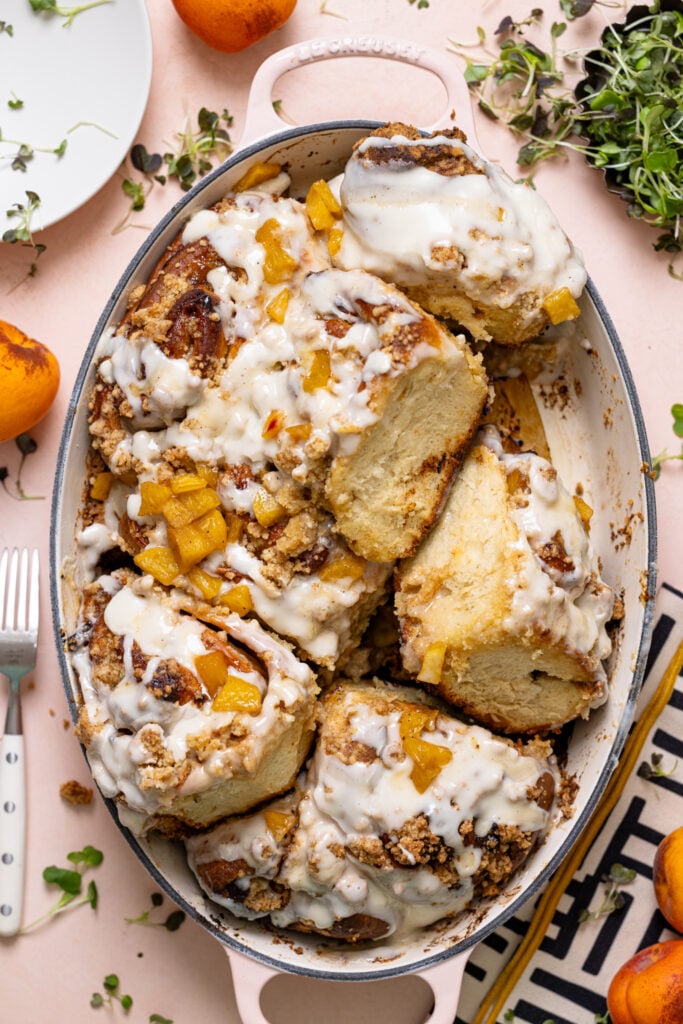 Southern Peach Cobbler Cinnamon Rolls in a baking dish with peaches and white plates.