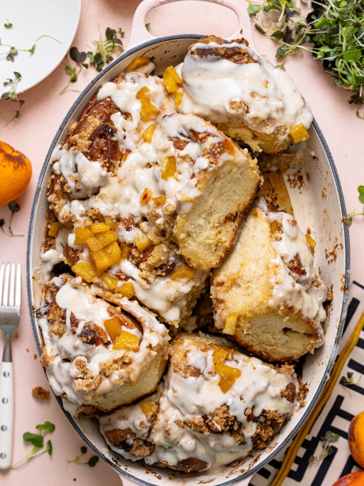 Southern Peach Cobbler Cinnamon Rolls in a baking dish with peaches and white plates.