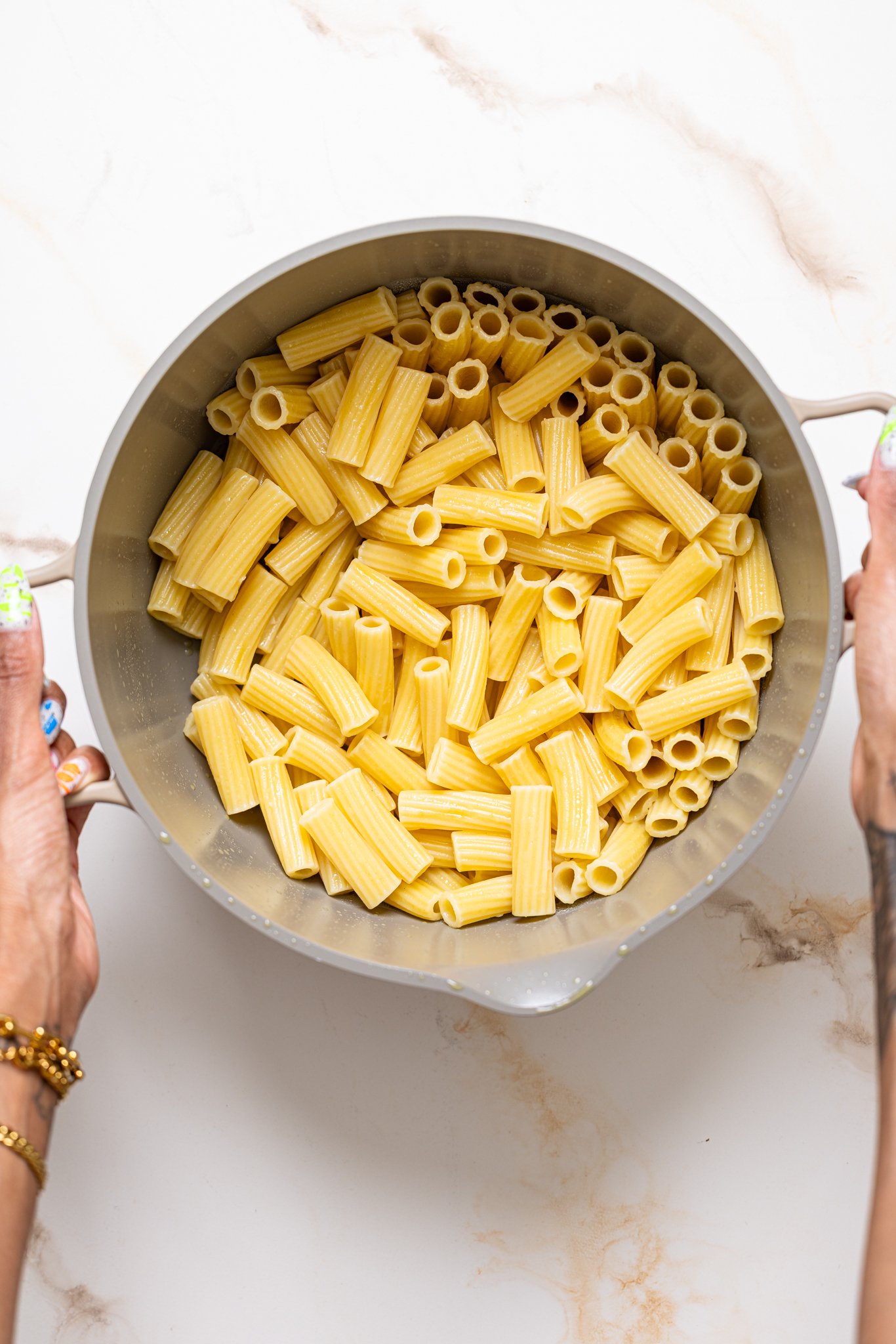 Cooked pasta in a pot being held by woman hands.