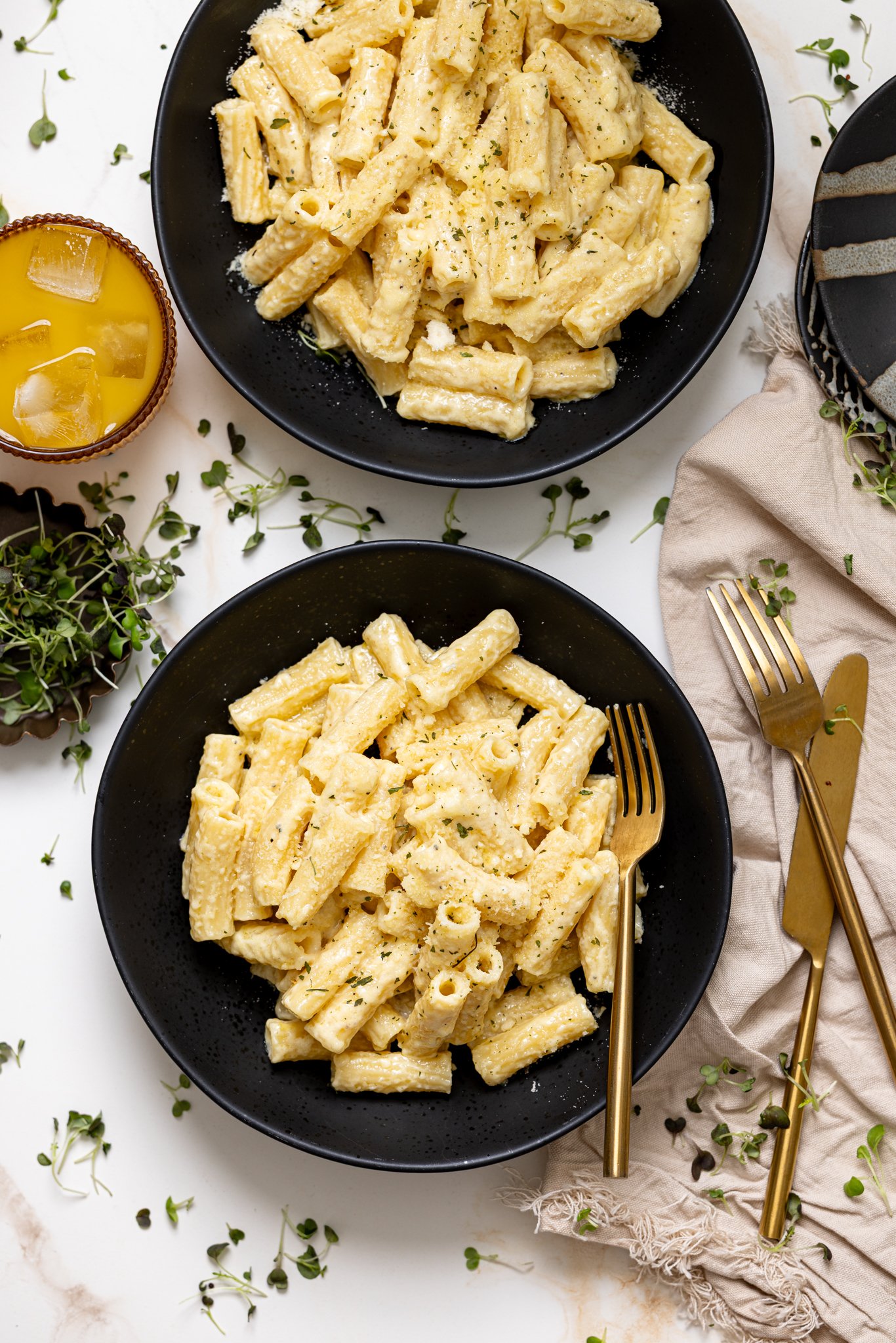 Creamy Weeknight Alfredo Pasta in bowls with utensils and a drink.