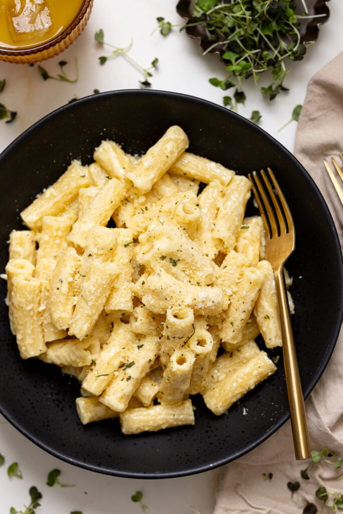 Creamy Weeknight Alfredo Pasta in a black bowl with a fork and drink.