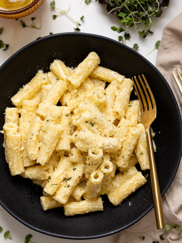 Creamy Weeknight Alfredo Pasta in a black bowl with a fork and drink.