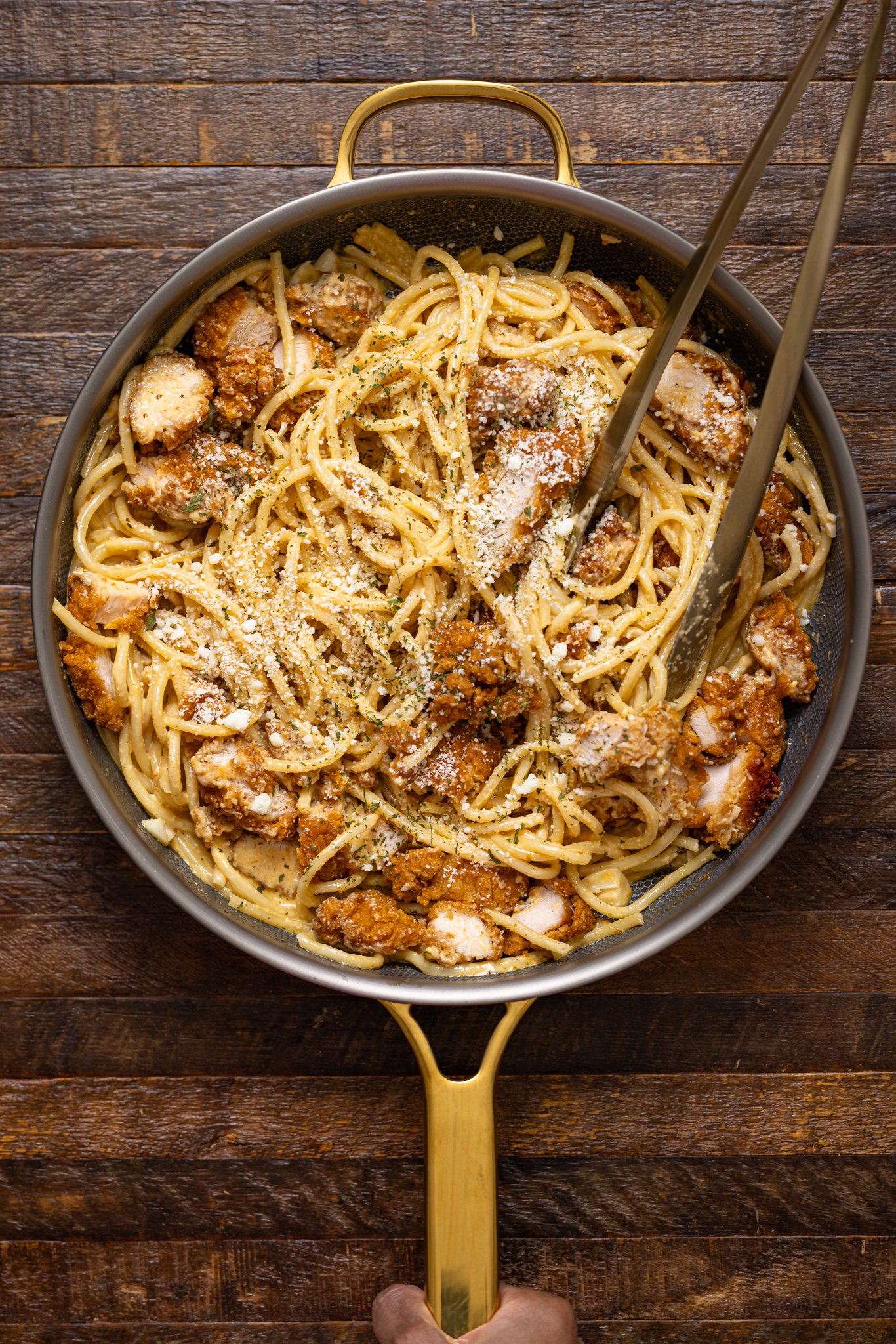 Southern Creamy Parmesan Garlic Chicken Pasta in a skillet with tongs being held by hands.