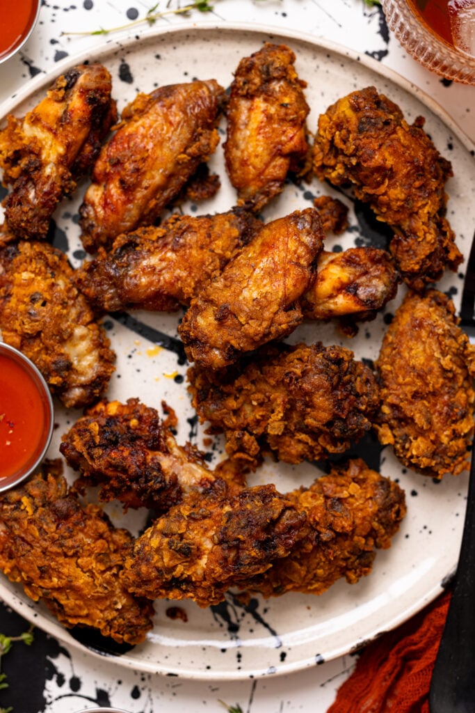 Up close shot of Crispy Spicy Fried Chicken Wings on a plate with hot sauce.