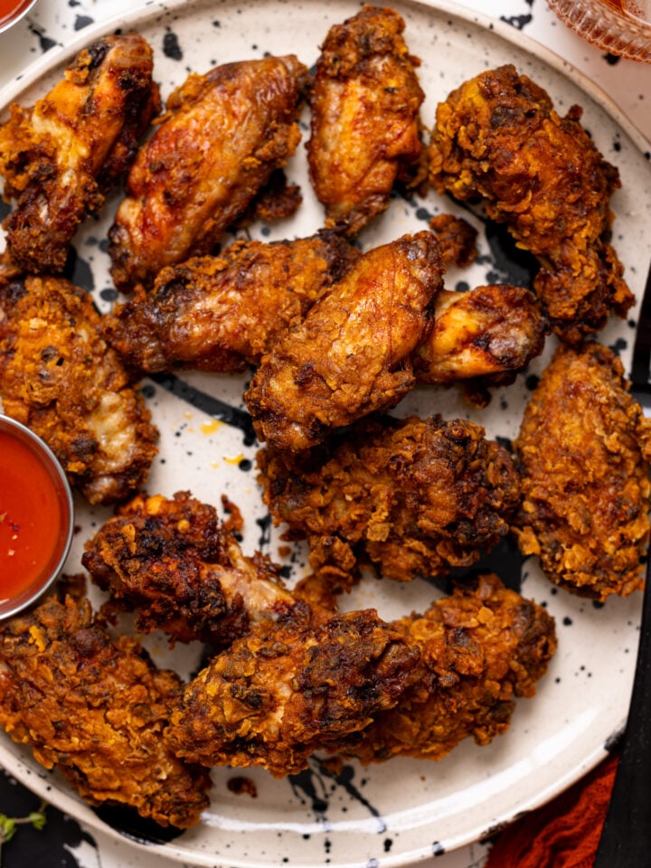Up close shot of Crispy Spicy Fried Chicken Wings on a plate with hot sauce.