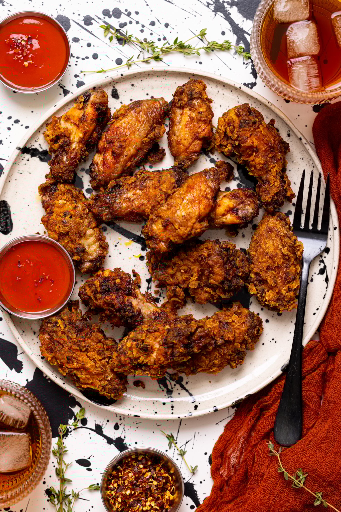 Crispy Spicy Fried Chicken Wings on a plate with a fork, hot sauce, and drinks.