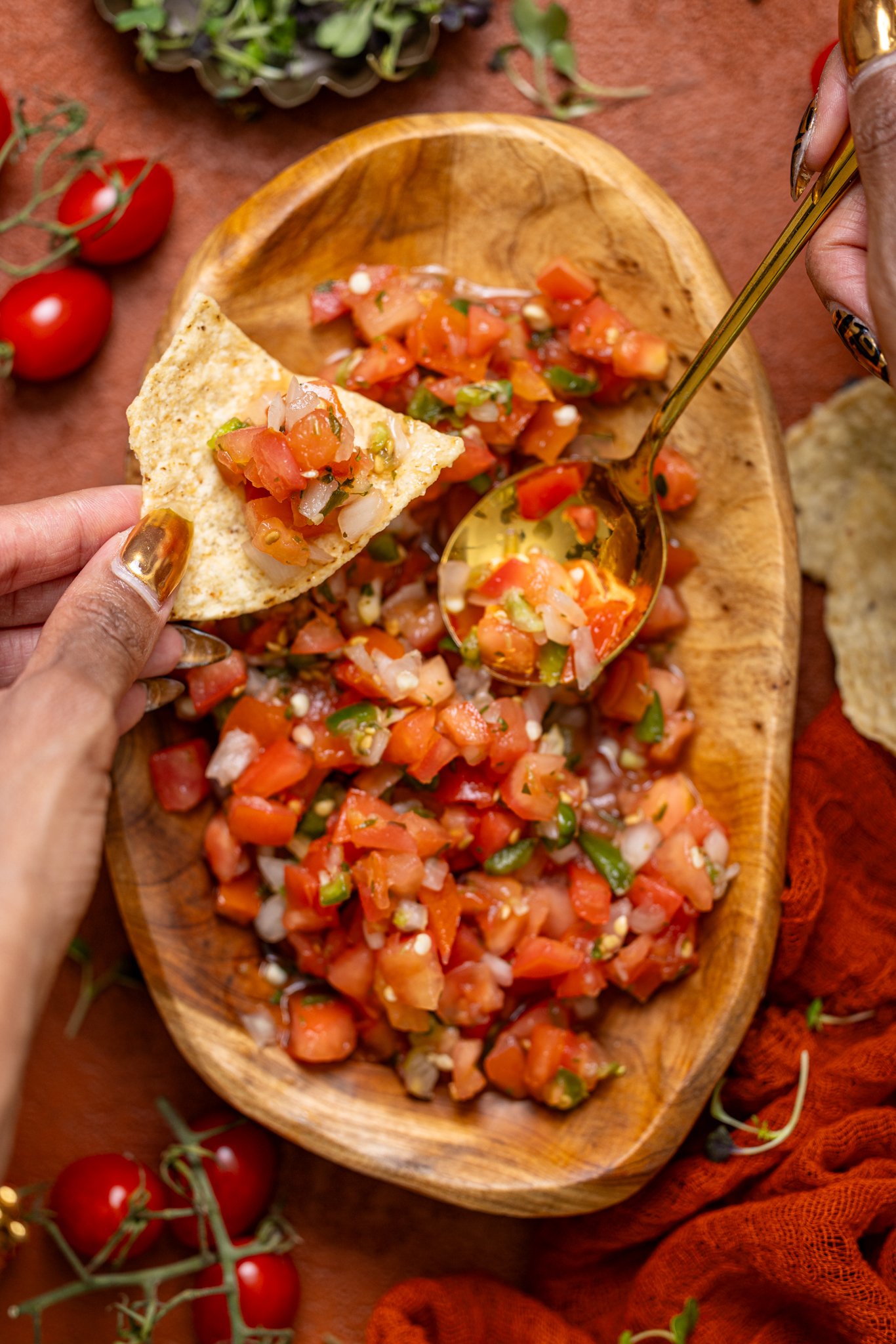 Fresh Pico de Gallo in a wooden bowl with a spoon and chips held by a woman's hand.