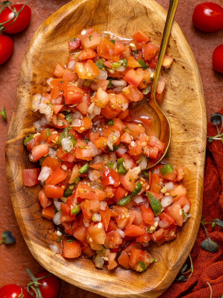 Up close shot of Fresh Pico de Gallo in a wooden bowl with a spoon.