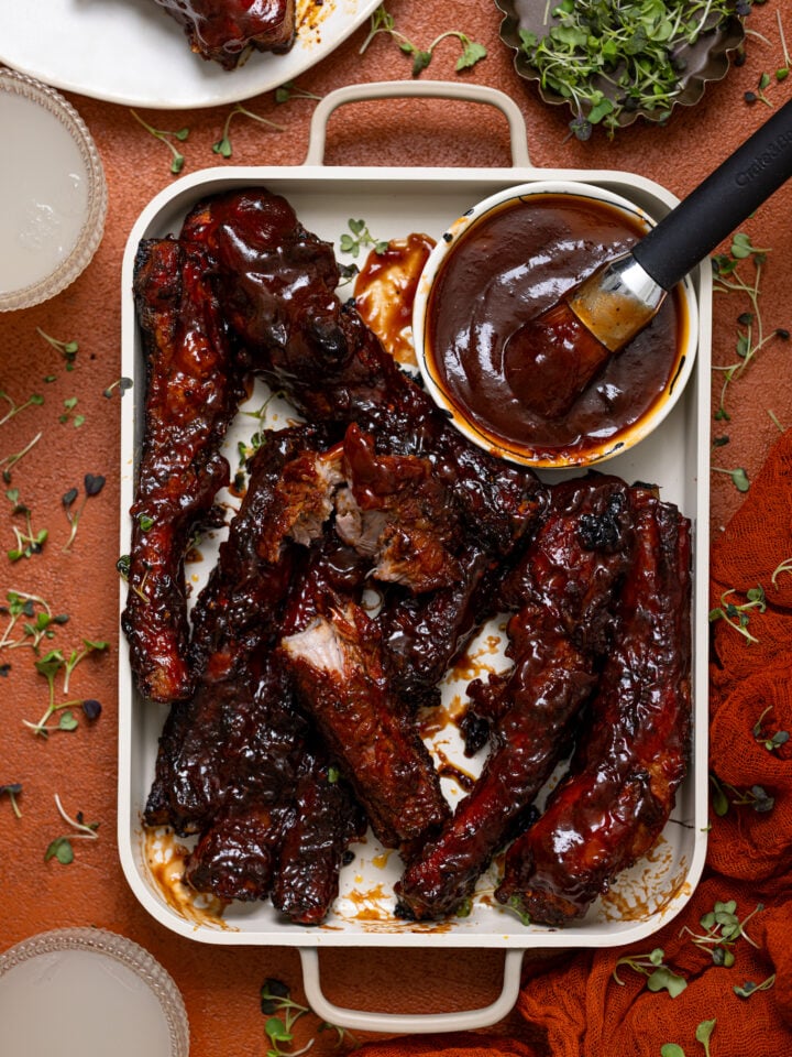 Hubby’s Favorite Oven-Baked BBQ Ribs on a burnt orange table with drinks and a plate of ribs.