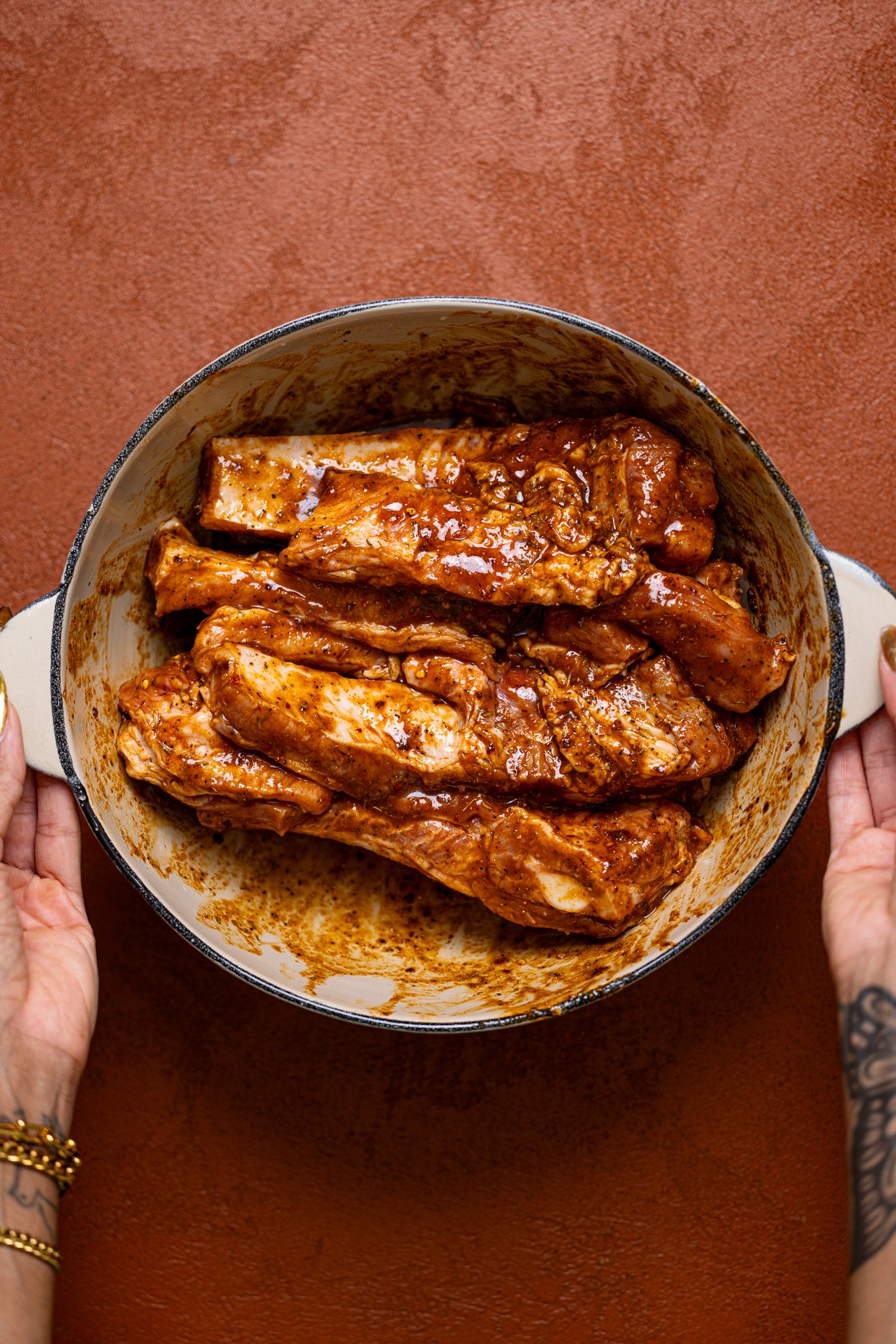 Seasoned ribs in a bowl being held by woman hands.