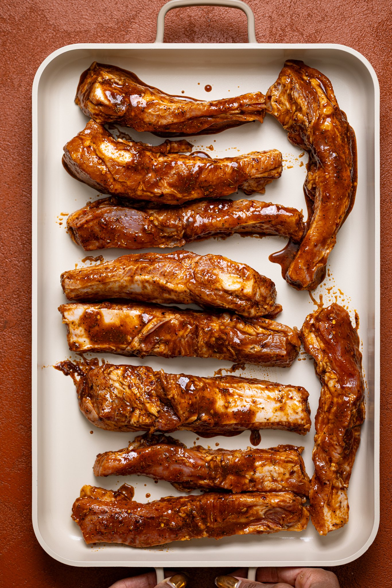 Seasoned ribs lined on a ceramic baking sheet.