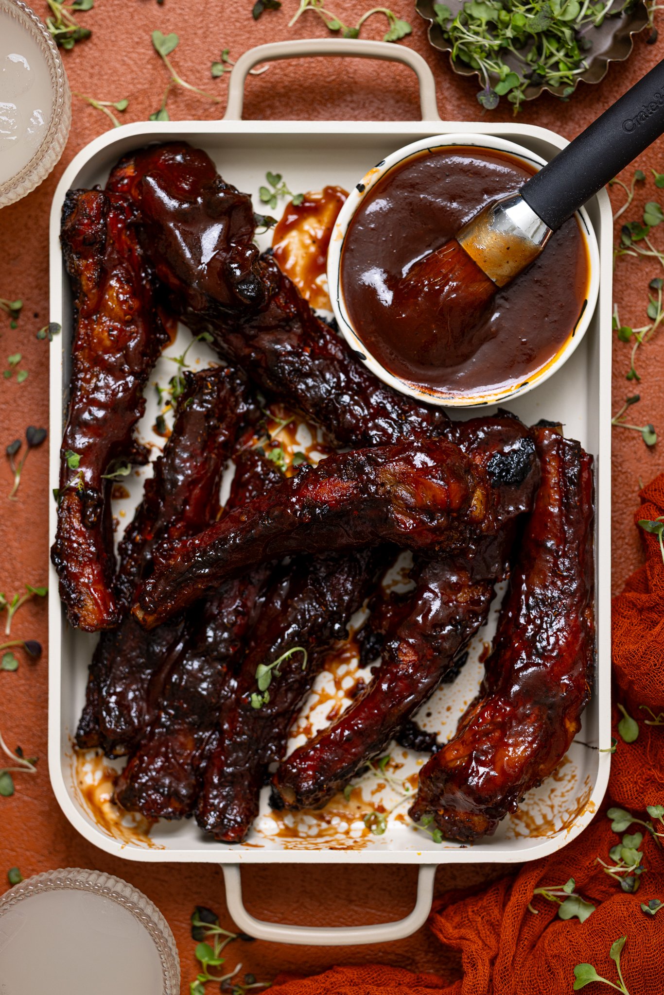 Hubby’s Favorite Oven-Baked BBQ Ribs on ceramic baking sheet with a side of drinks.
