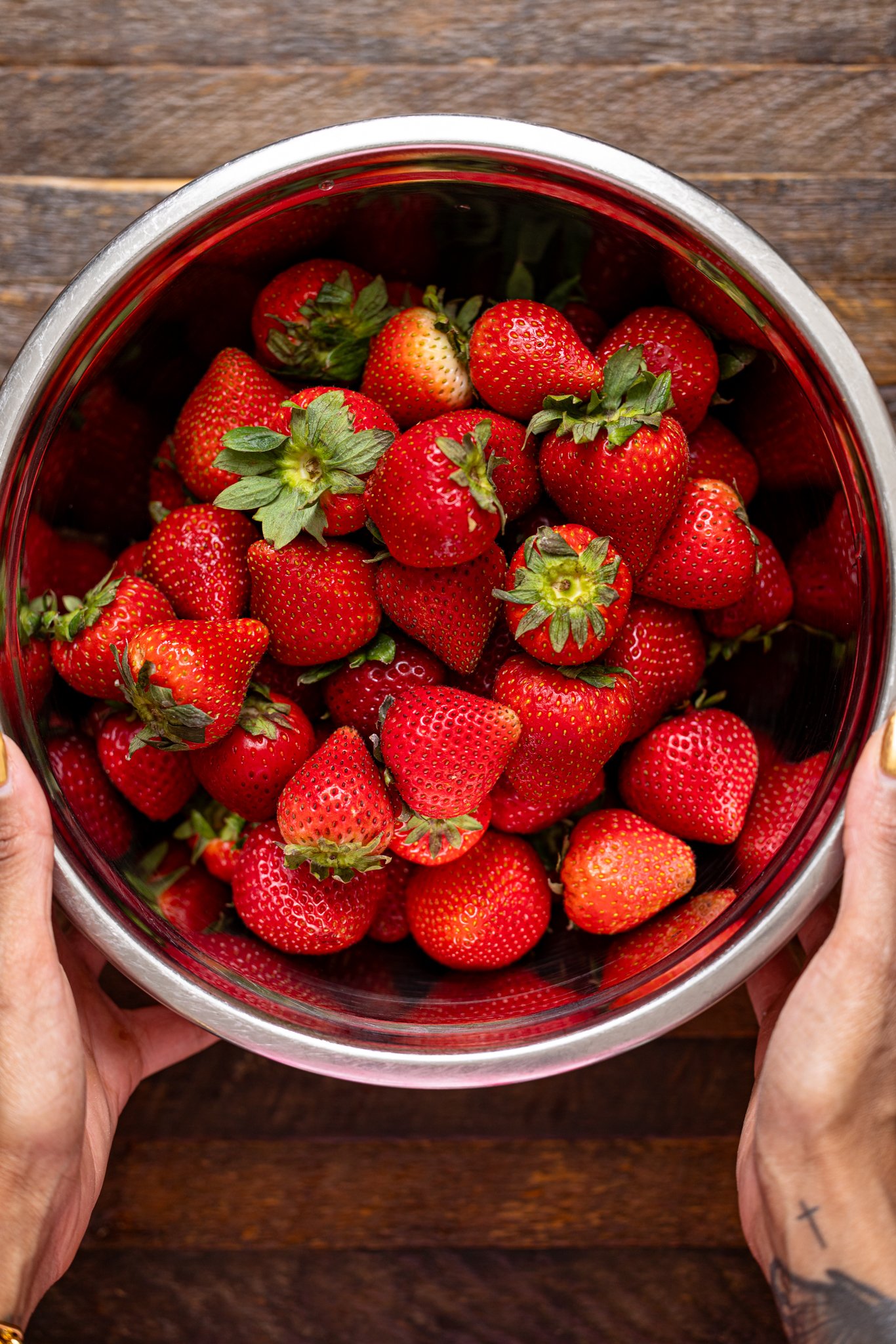 Strawberries in a silver bowl being held by woman hands.